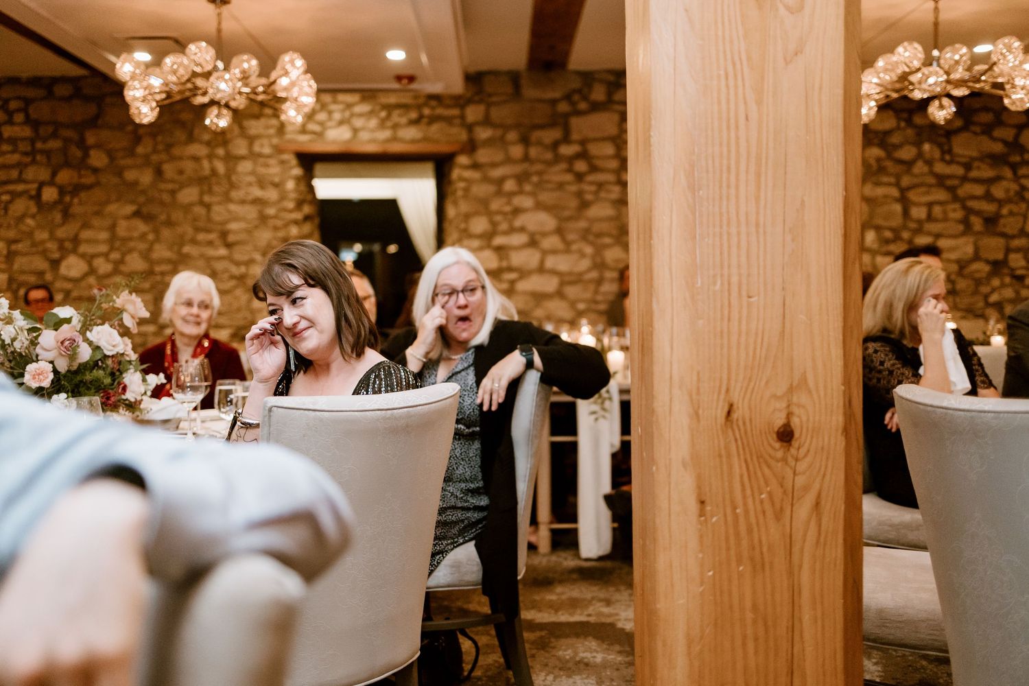Reception venue featuring stone walls, wooden pillars, and elegant white chairs.