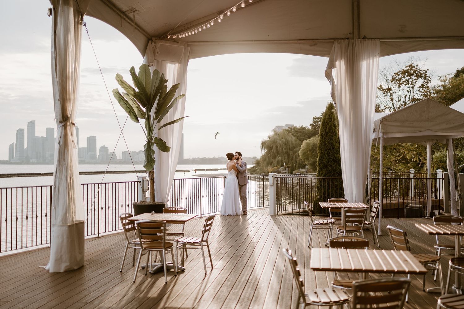 Covered outdoor wedding venue with wooden furniture overlooking waterfront views.