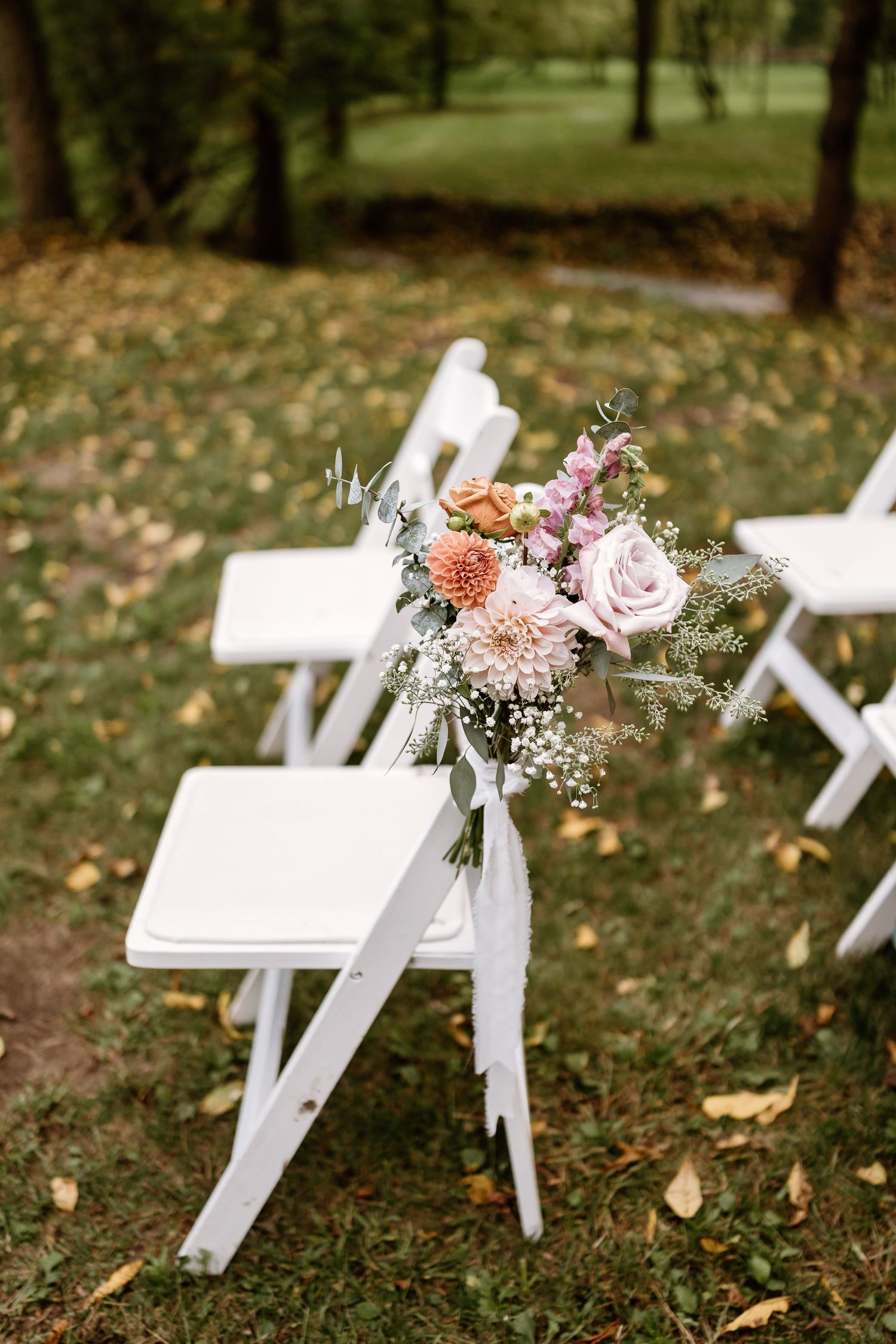 White folding chairs decorated with delicate floral arrangements set up for an outdoor wedding ceremony.