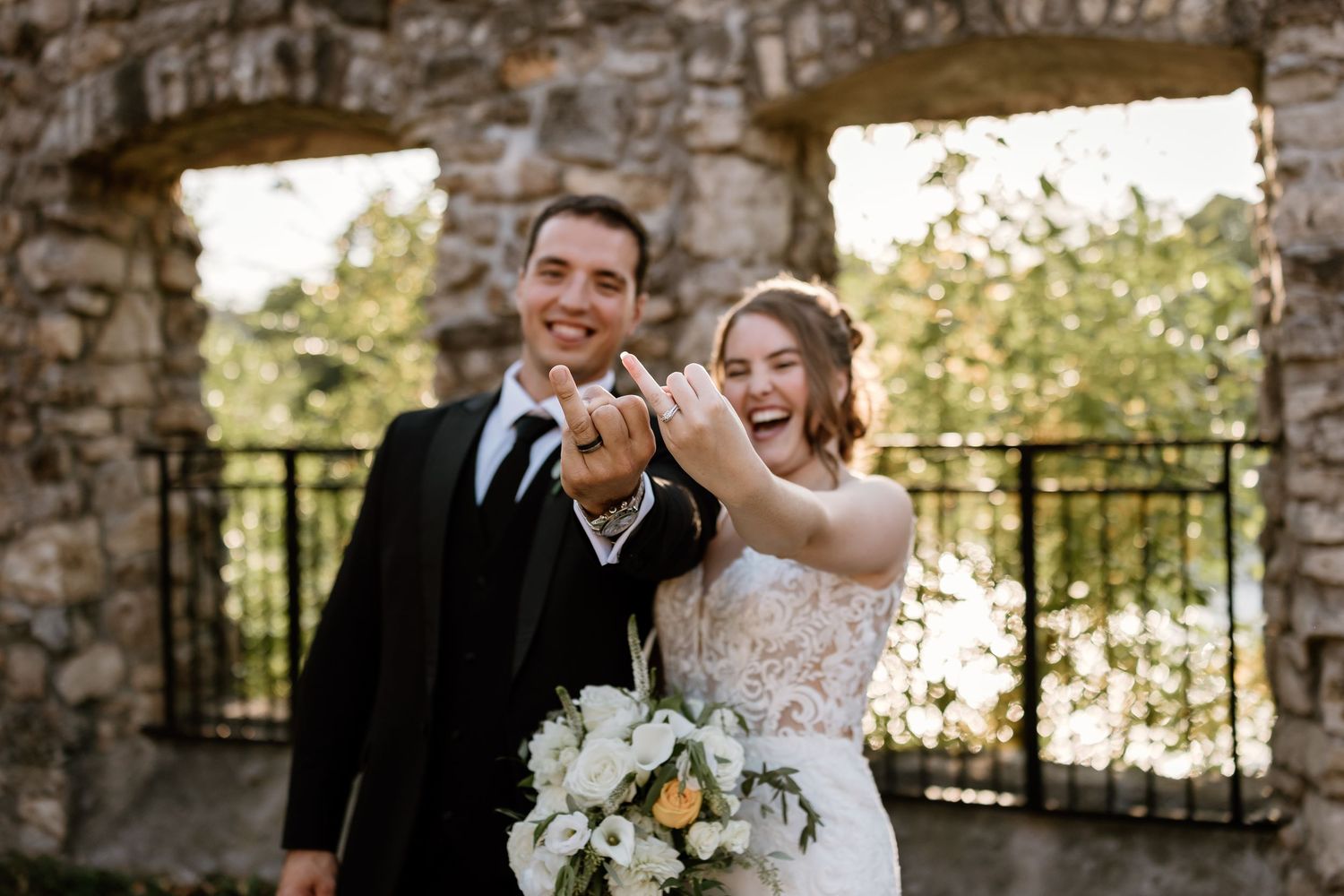 Romantic wedding couple embracing at sunset on stone steps with white floral bouquet.