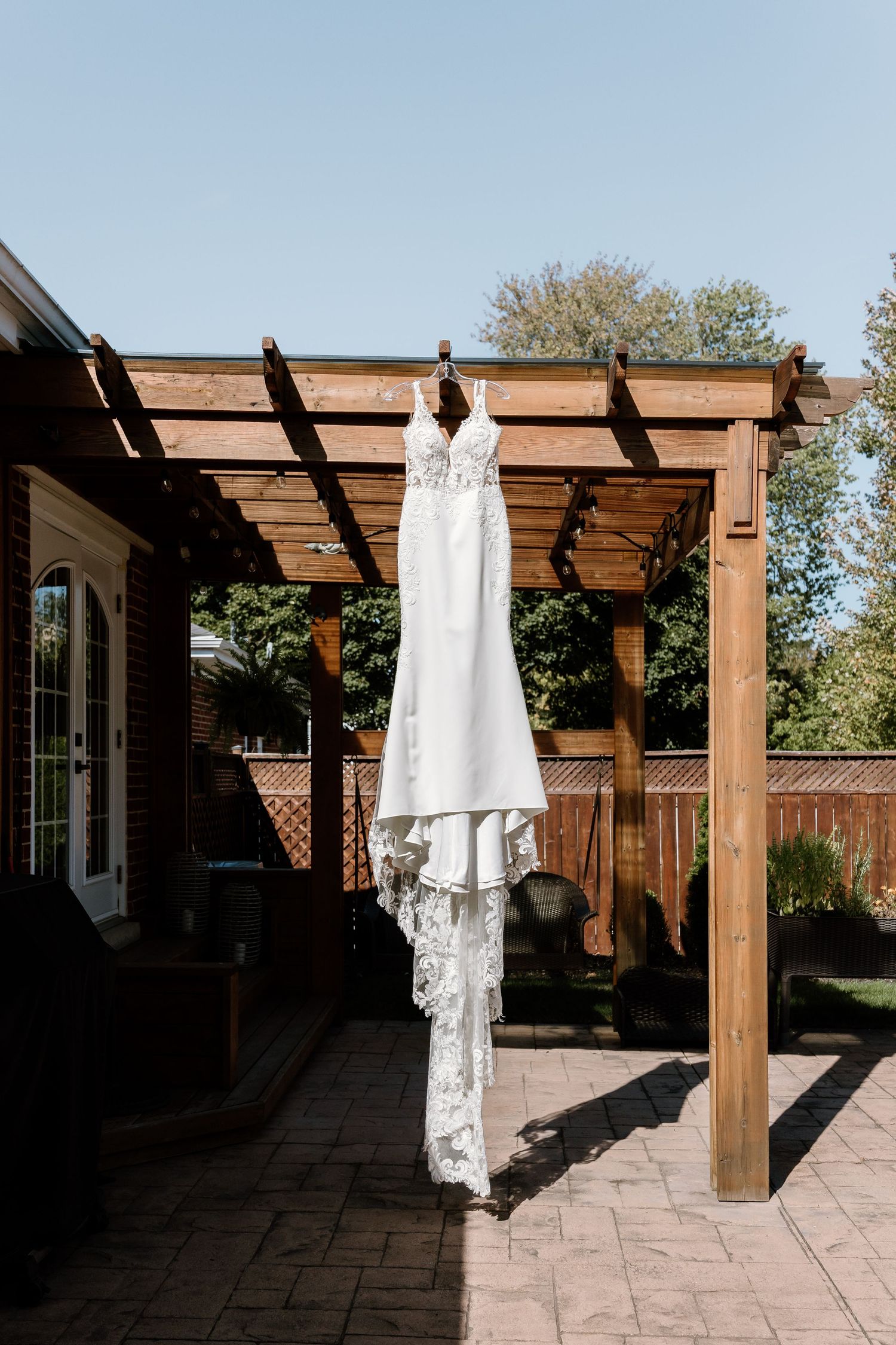 White wedding dress hanging from wooden pergola in outdoor garden setting.