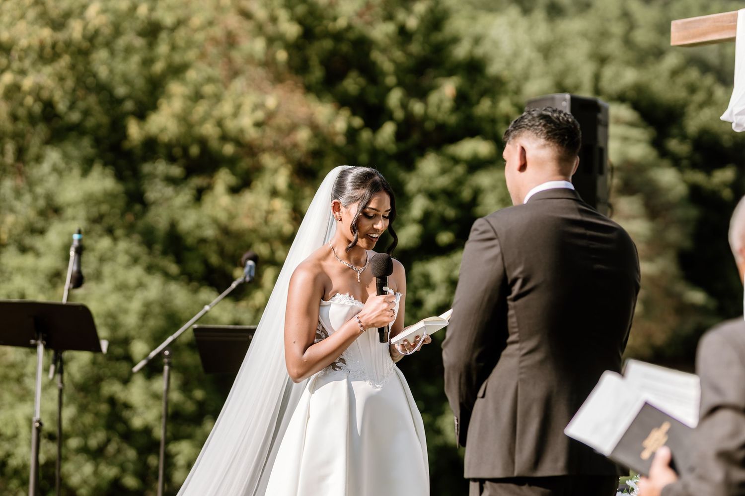 A couple exchanges vows during their outdoor wedding ceremony with microphones visible.