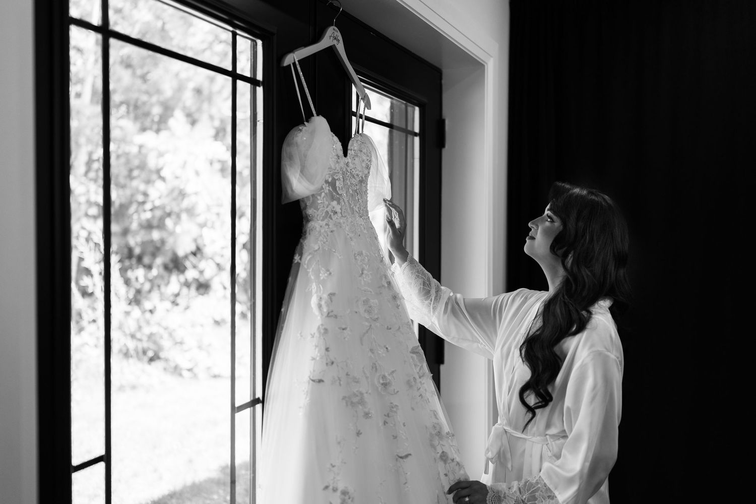 Wedding dress hanging in window light creating dramatic silhouette.