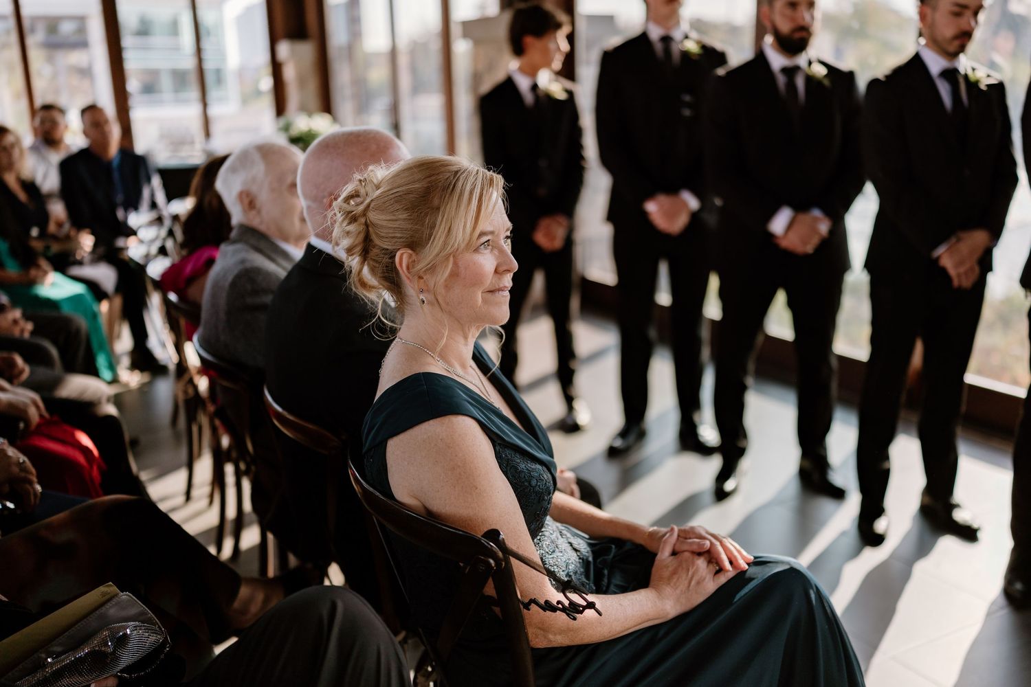 Wedding guests seated during ceremony with groomsmen standing in background.