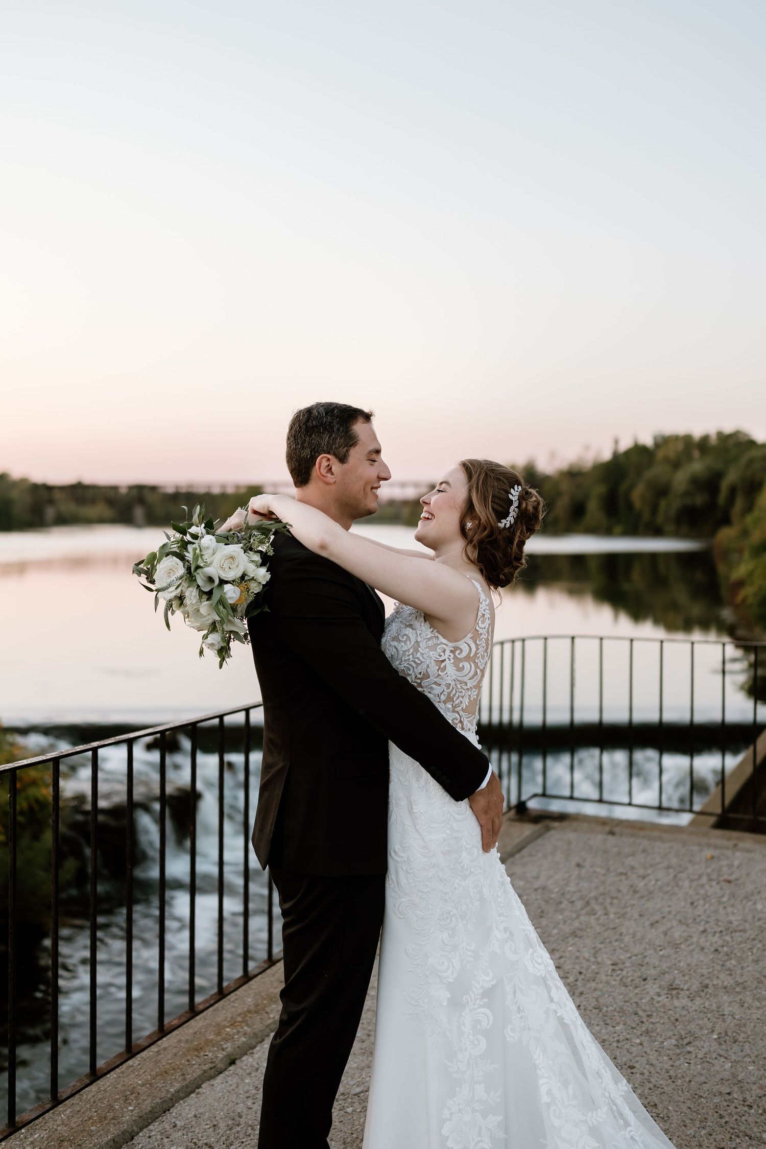 Romantic sunset wedding photos by lake with couple dancing on stone patio.