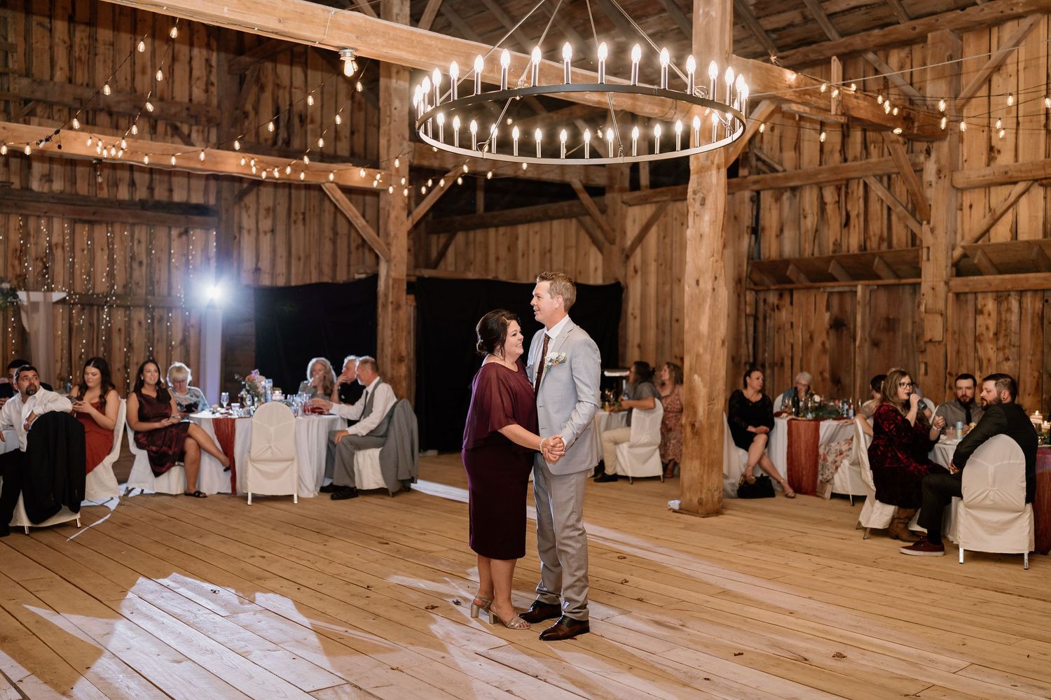 Panoramic view of a barn wedding reception with string lights and wooden beams creating an elegant atmosphere.