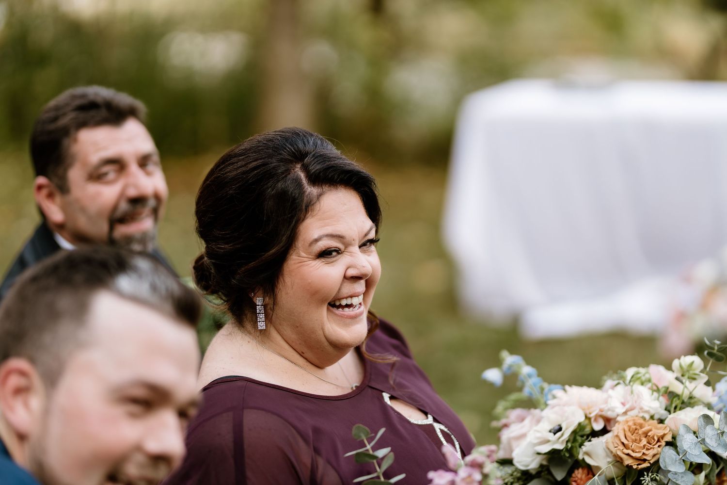 Wedding party members share joyful moment during outdoor ceremony.