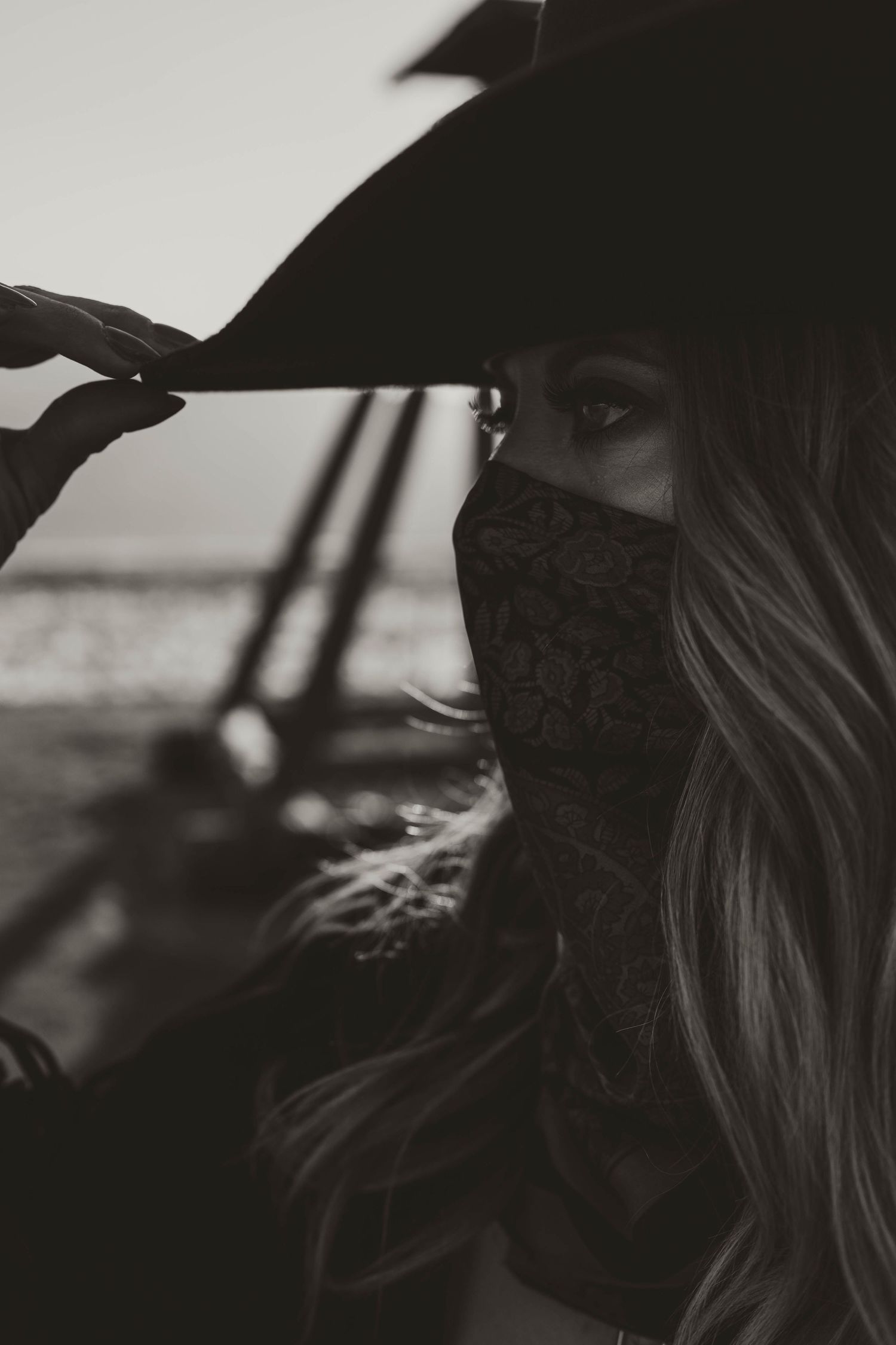 Black and white portrait of a masked figure with long flowing hair in dramatic lighting.
