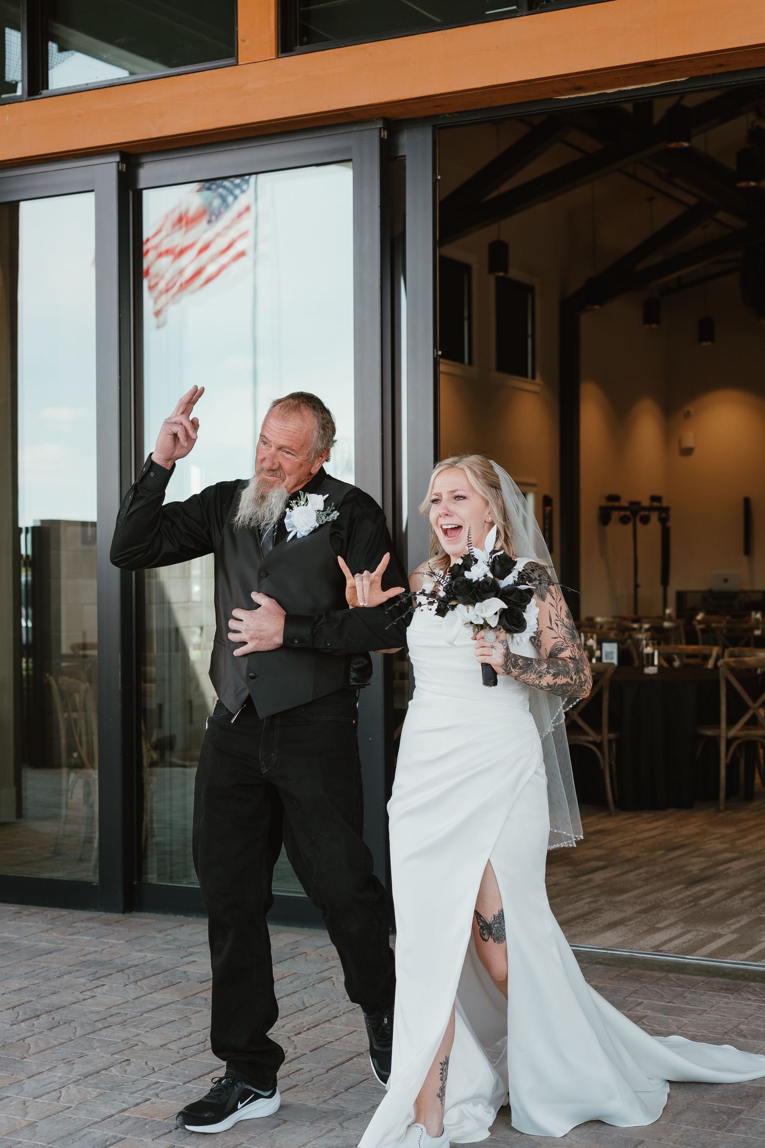 Bride and groom celebrate their wedding entrance outdoors, making rock hand gestures, bride holding bouquet in white gown with veil.