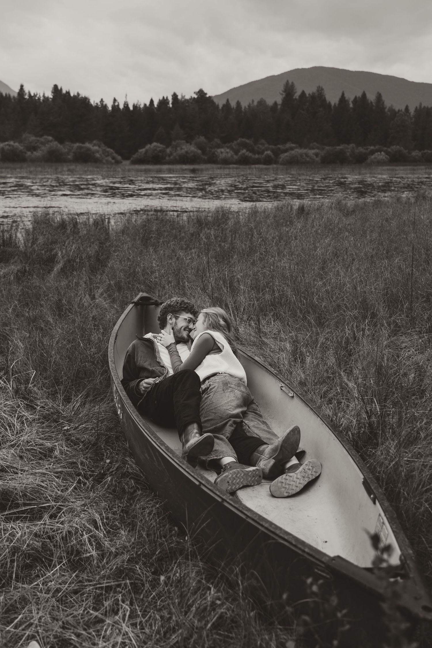 A sequence of black and white photos showing a couple resting together in a canoe among tall grasses near a lake.