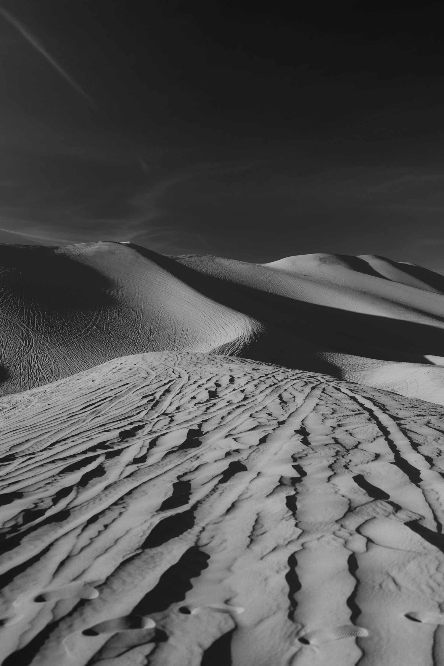 Black and white desert landscape with dramatic sand dunes and rippling patterns carved by wind in the sand.