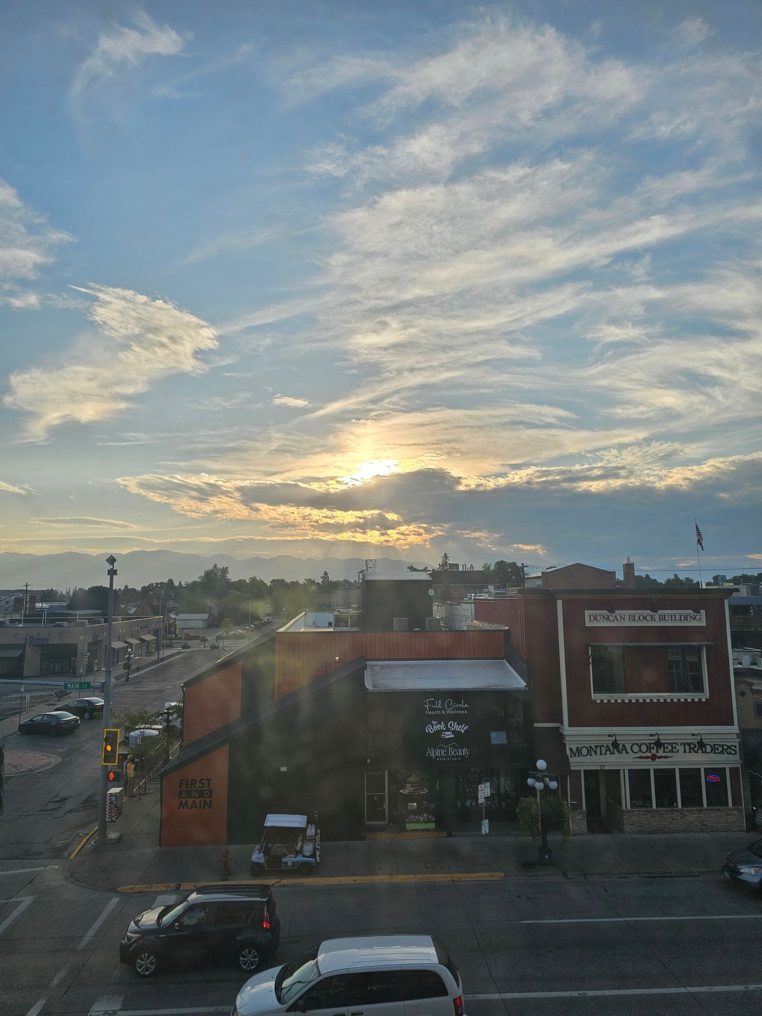 Panoramic sunset view over small town storefronts with dramatic clouds and golden light streaking across blue sky.