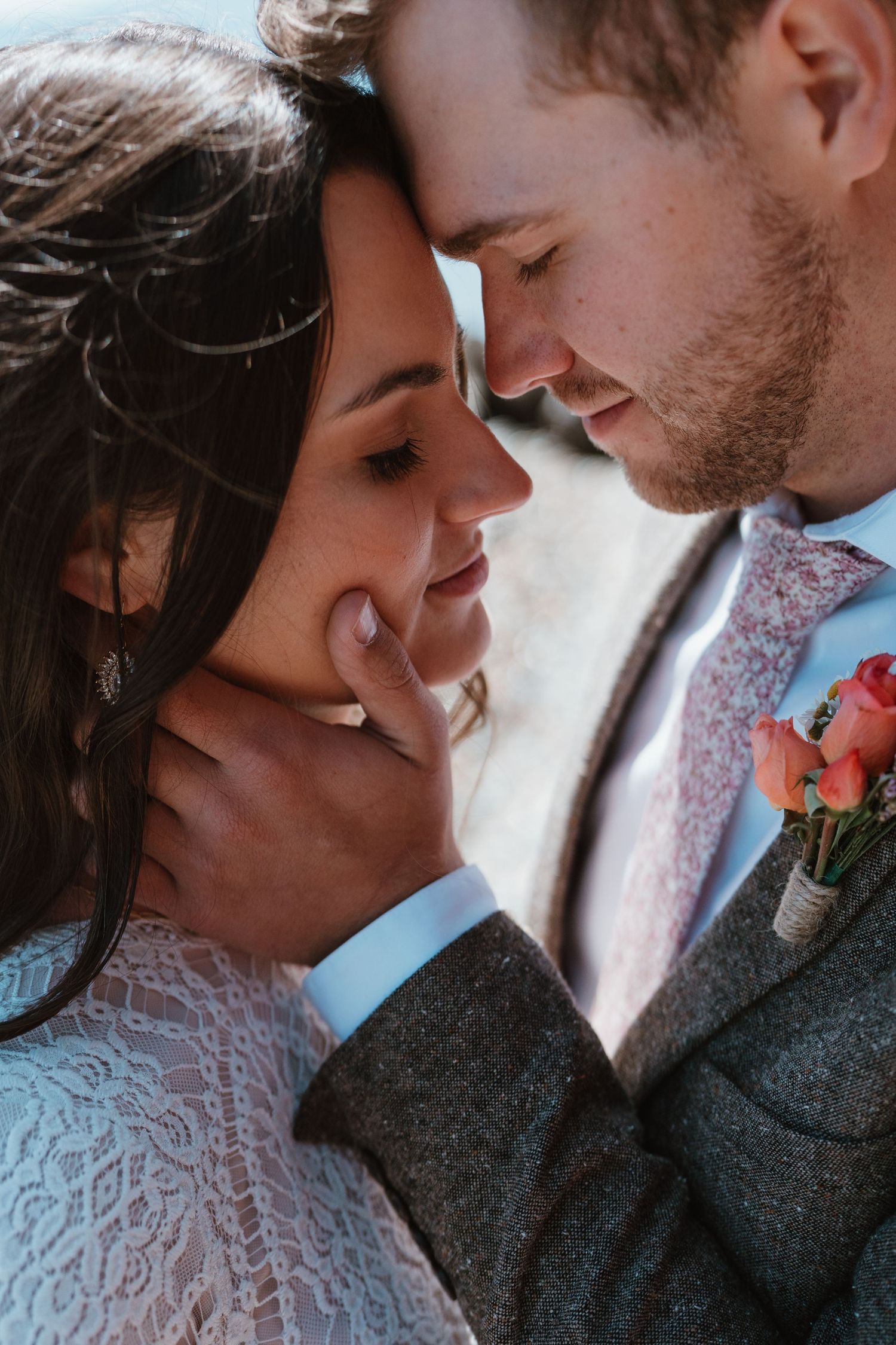 Groom tenderly cups bride's face as they lean foreheads together in an intimate wedding portrait close-up.