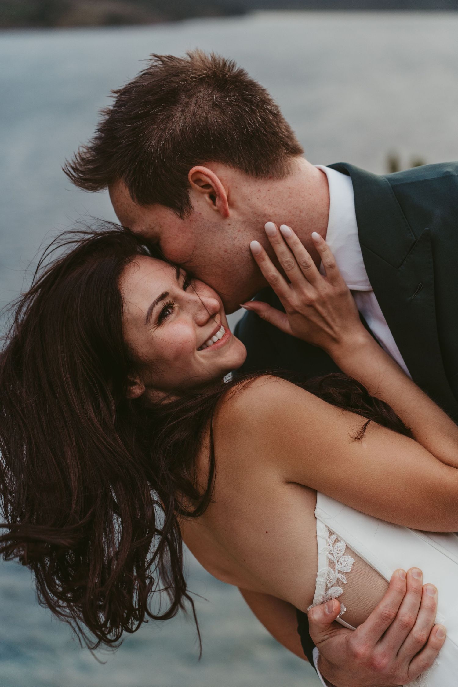 A romantic couple embraces and kisses in a series of intimate wedding photos by the water.