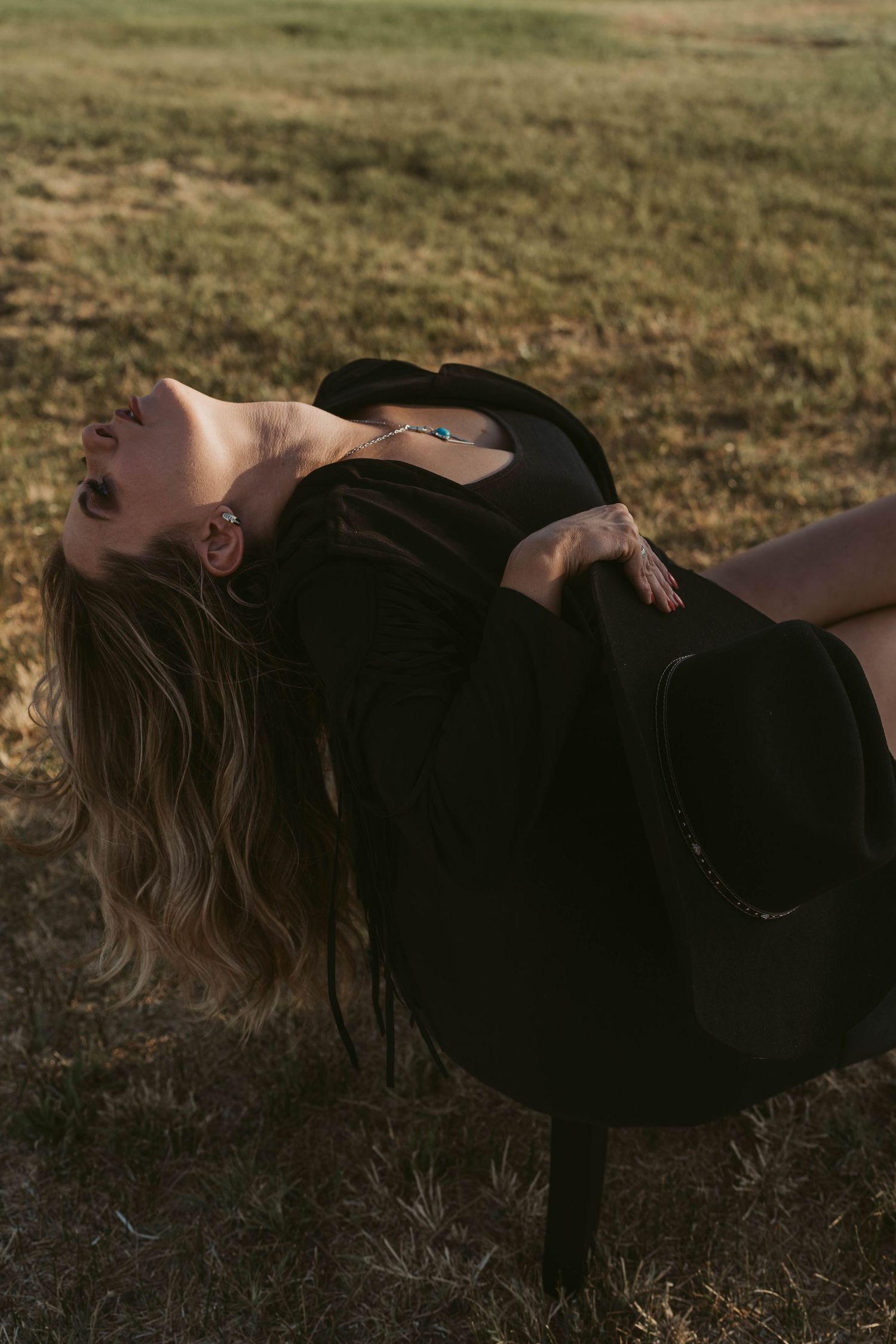 Person in black dress lying on grass during golden hour with hair spread out in artistic pose.