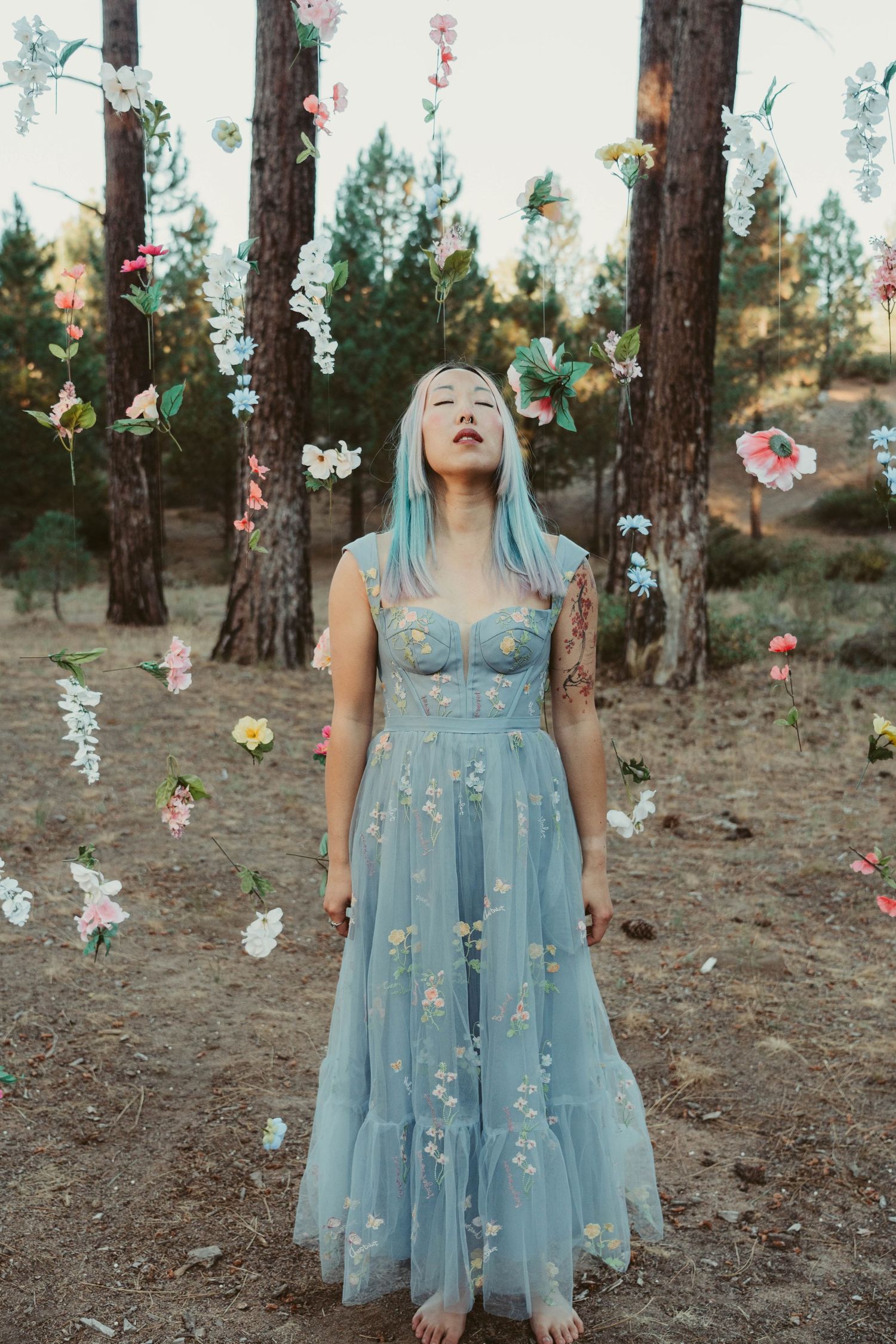 A dreamy forest scene with a light blue tulle dress and floating paper flowers creates an ethereal woodland atmosphere.