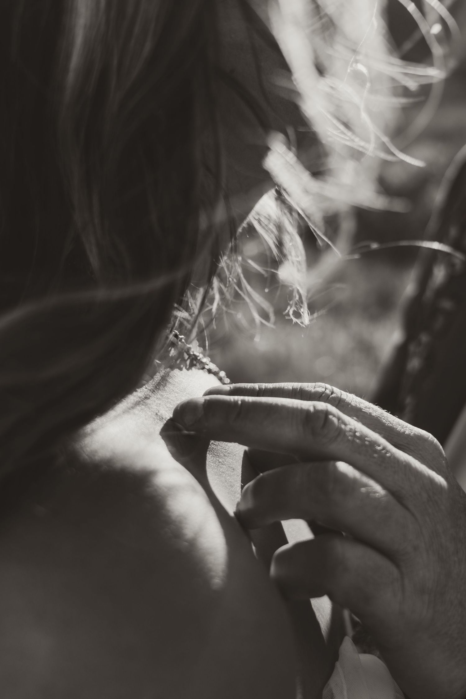 Close-up black and white photo of a hand with ring gently touching a womans hair in soft light.