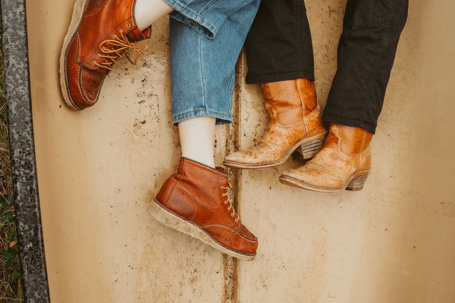 A couple wearing worn leather boots and shoes in brown and tan colors shown against a canoe.