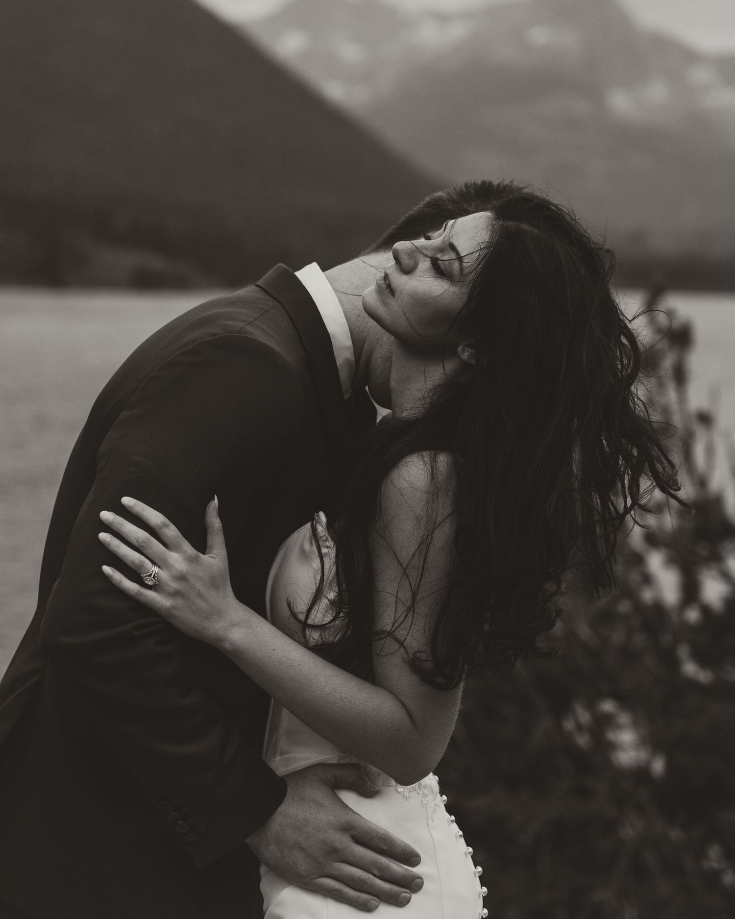 Wind swept elopement couple embracing near lake in Glacier National Park Montana.