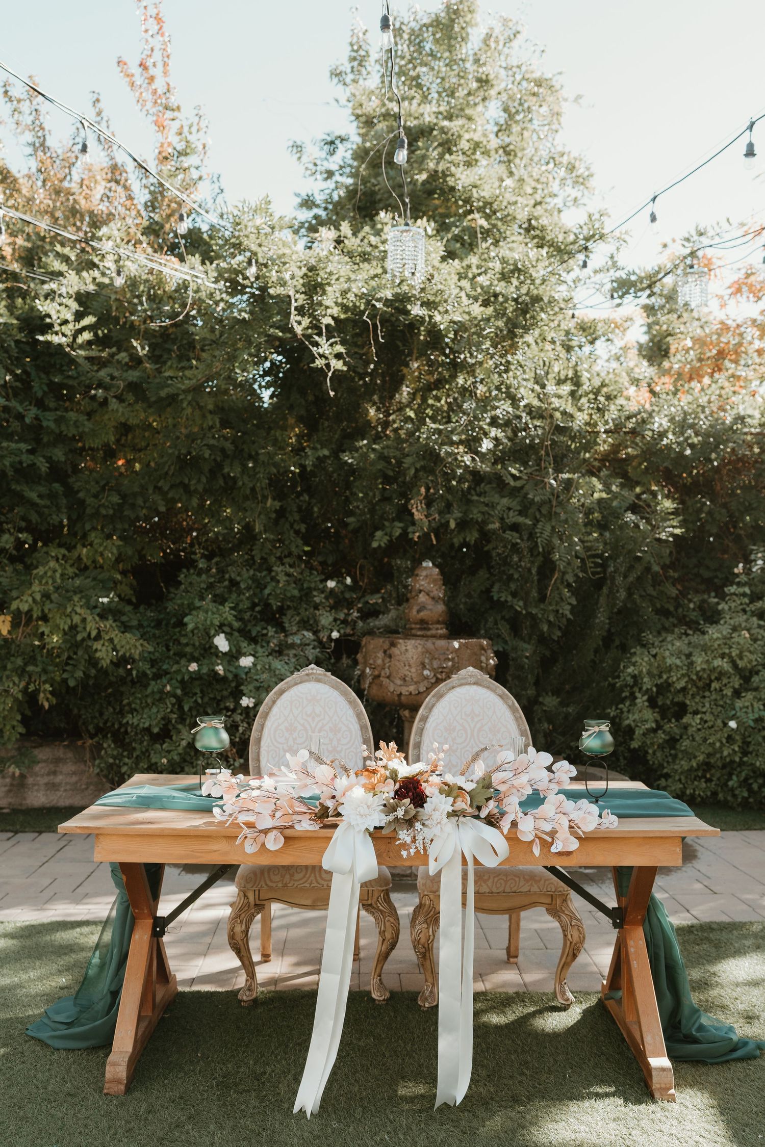 Rustic wooden benches decorated with white ribbons and floral arrangements set up for an outdoor garden wedding ceremony.