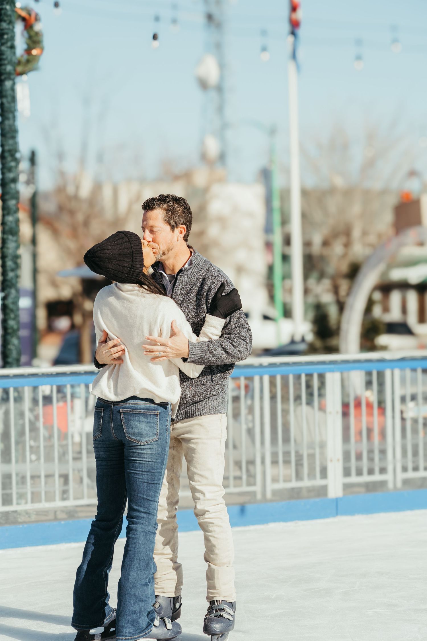 A couple shares a romantic moment while ice skating on an outdoor rink on a winter day.