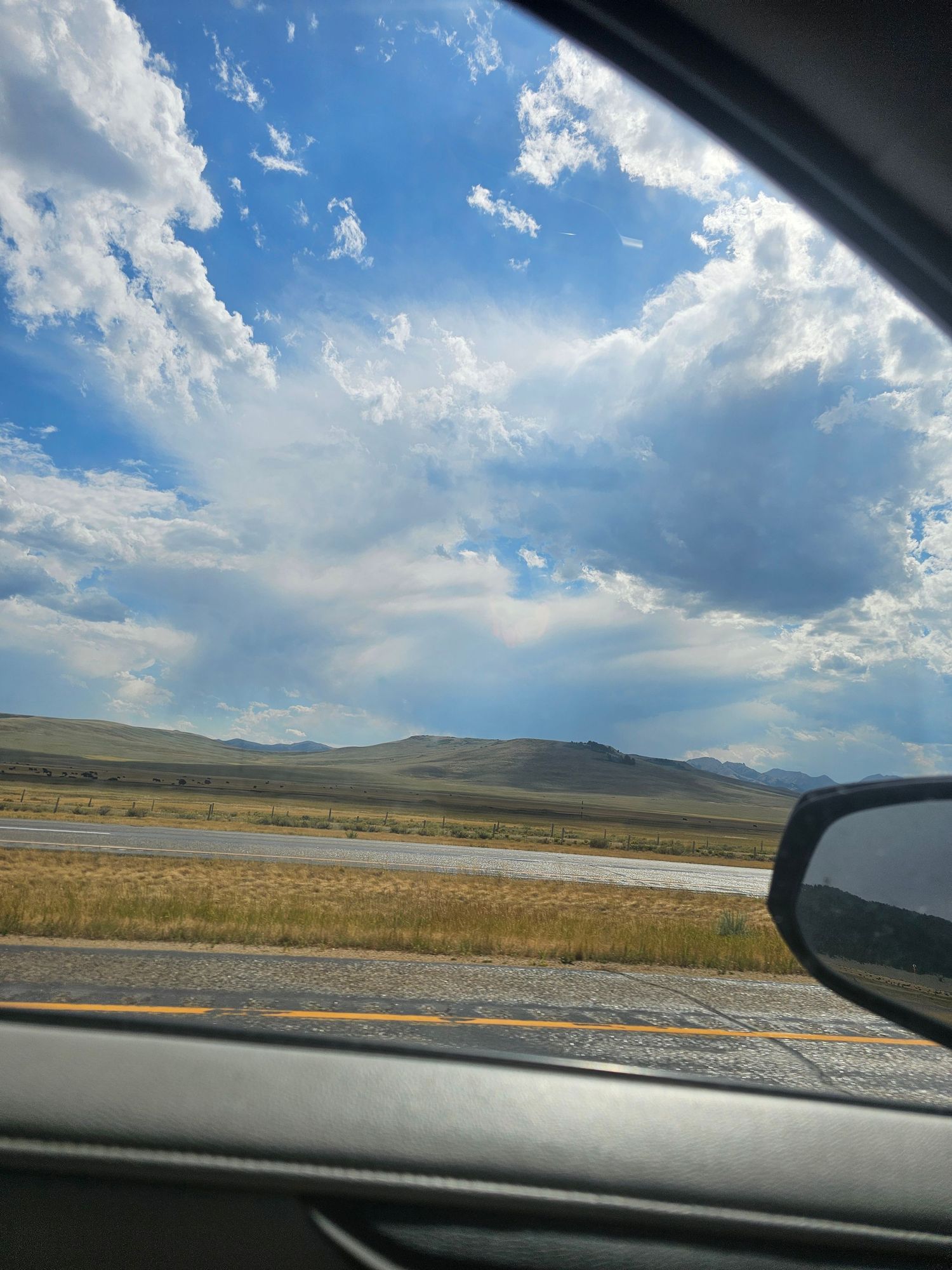 A panoramic sequence of rolling hills and blue skies with puffy white clouds viewed through a car windshield.