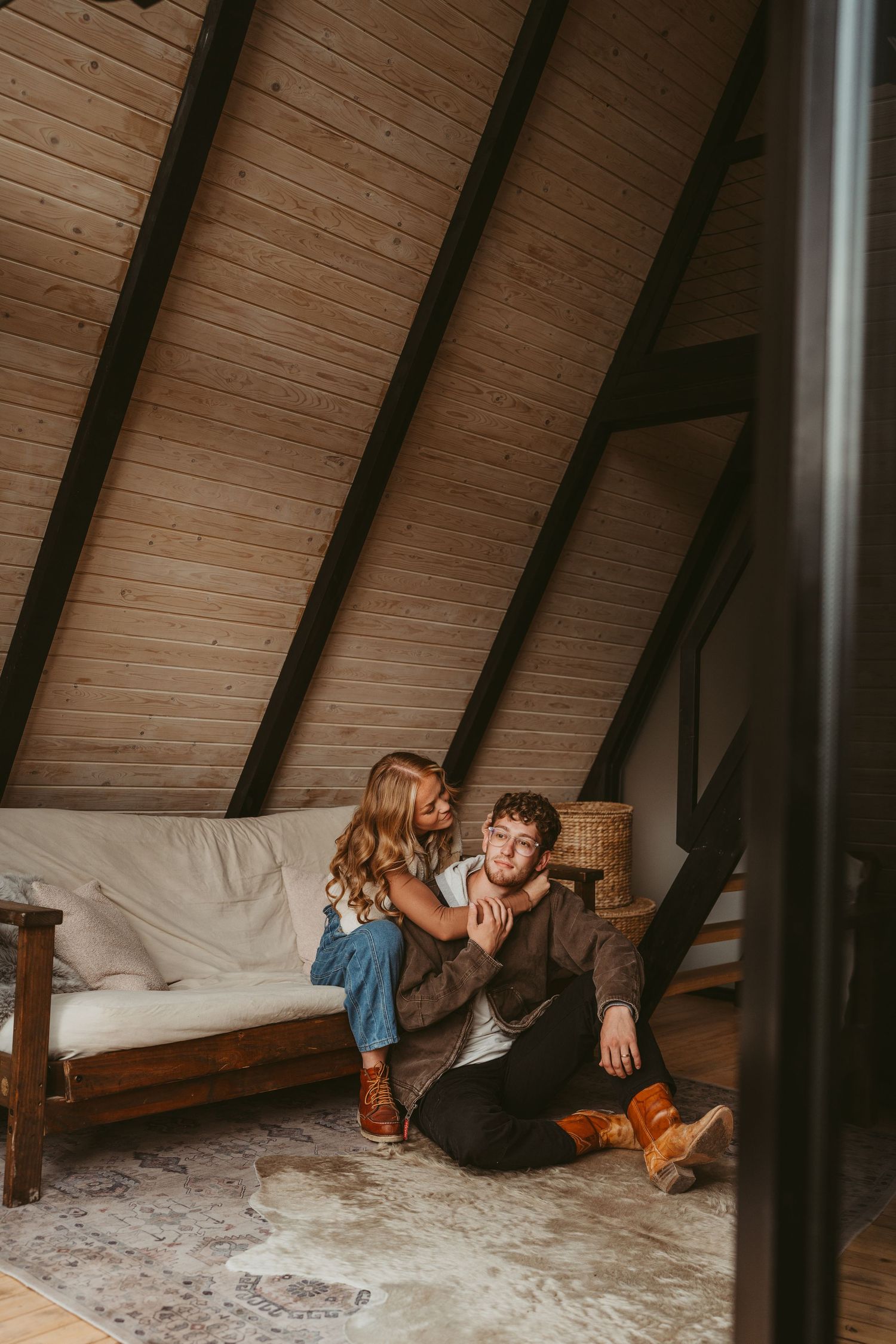 Couple relaxing together in cozy A-frame cabin loft with wooden beams and white bedding.