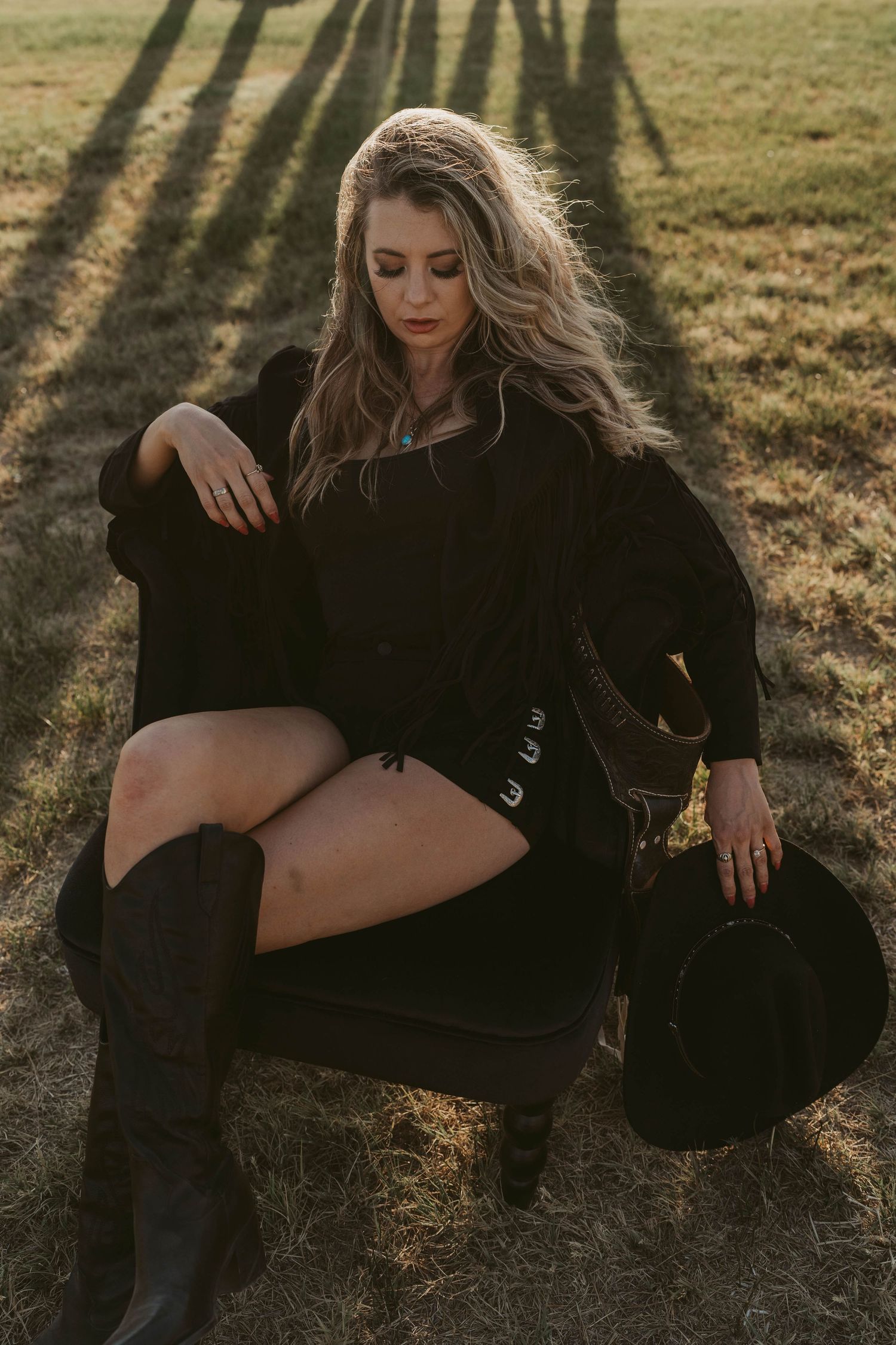 A person in black clothing poses artistically on grass during golden hour lighting.