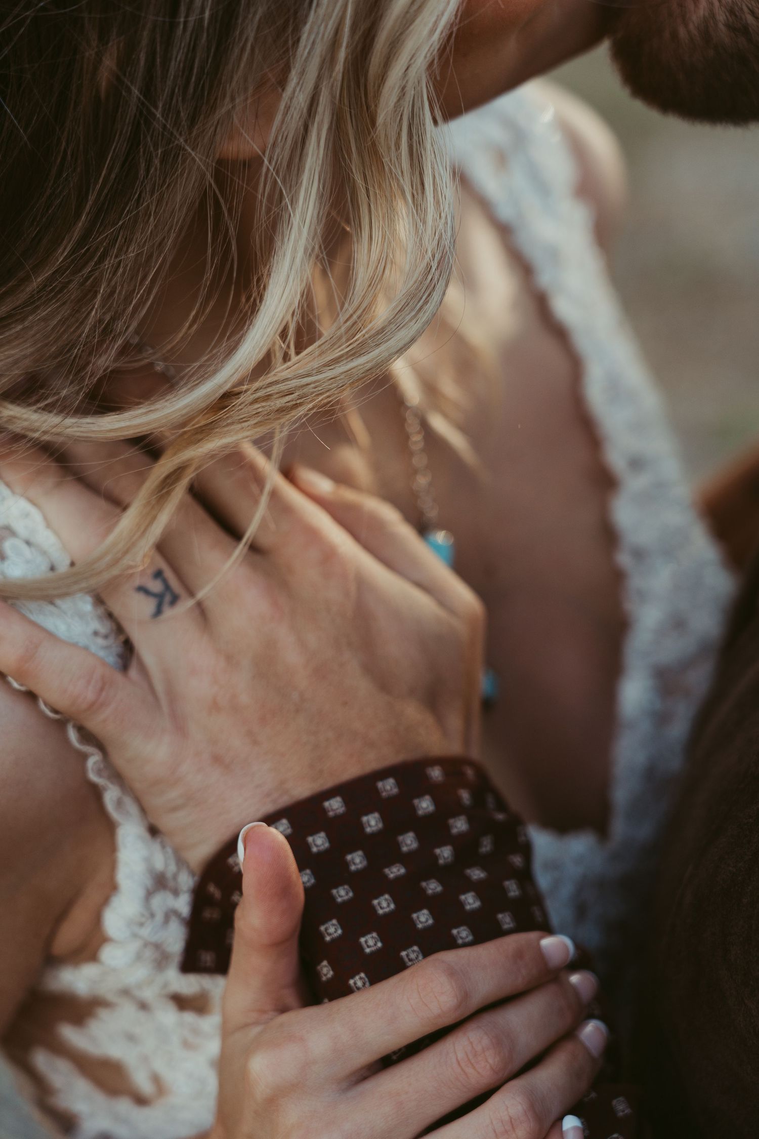 Close-up of a groom's hand tenderly holding a bride's neck, showcasing a small tattoo and lace wedding dress details.