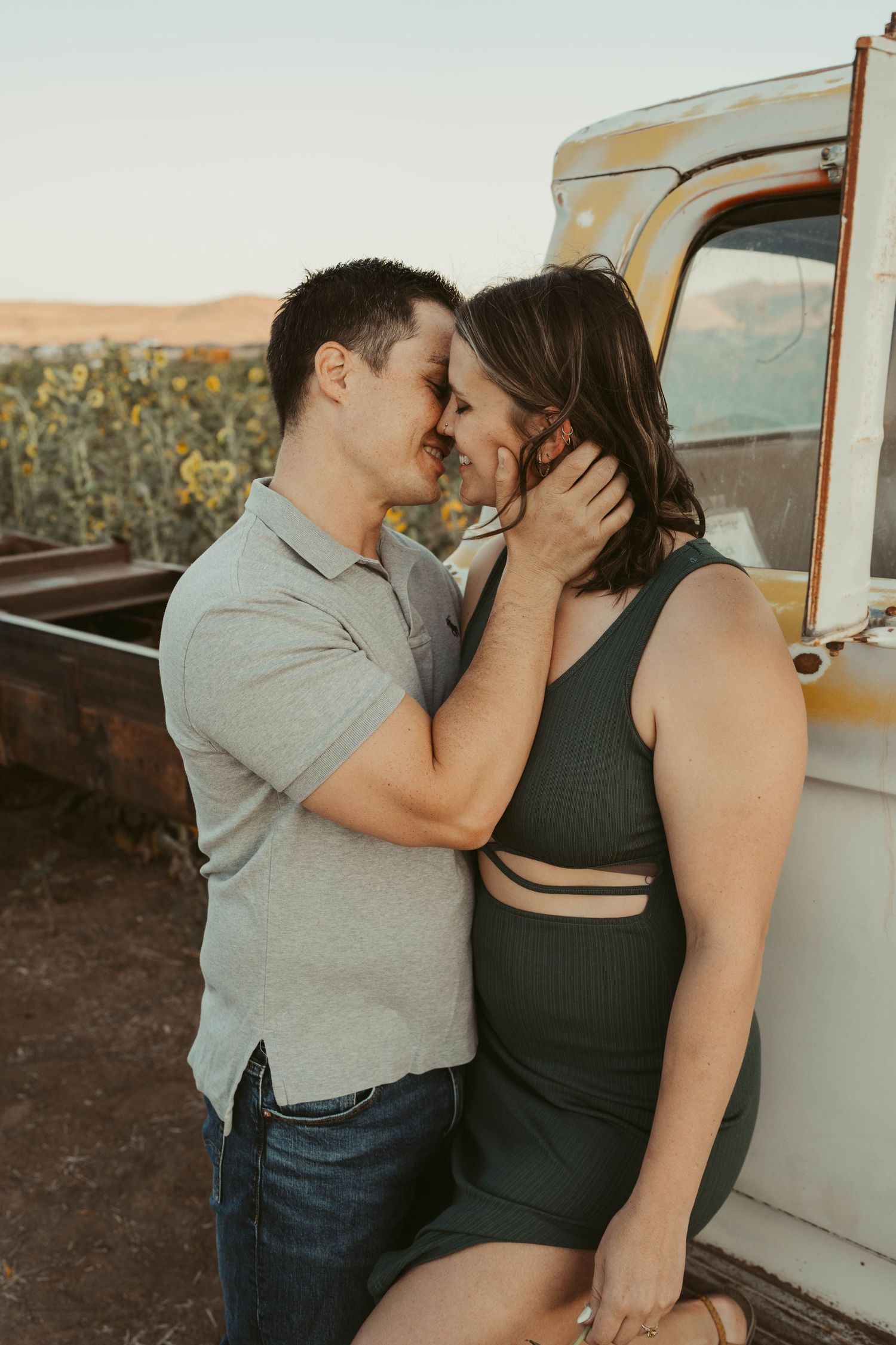 A romantic couple shares tender kisses next to a vintage white vehicle during a sunset photoshoot.