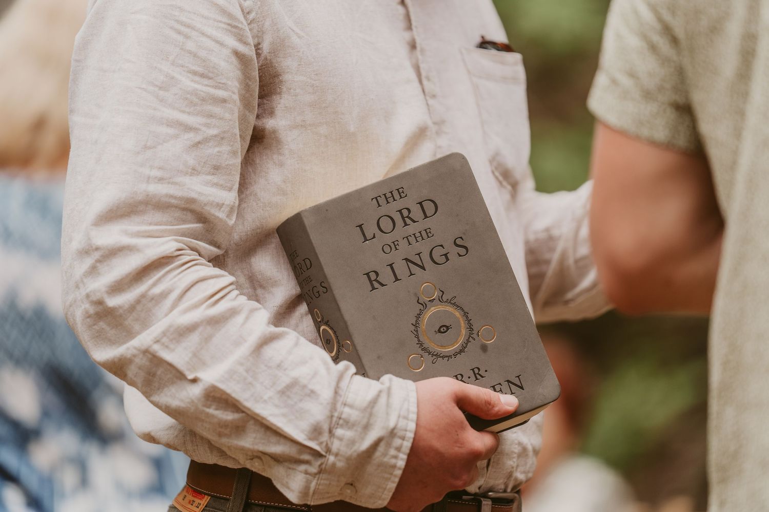 A person holds a worn copy of The Lord of the Rings book in their hand while wearing a white long-sleeved shirt to officiate a wedding.