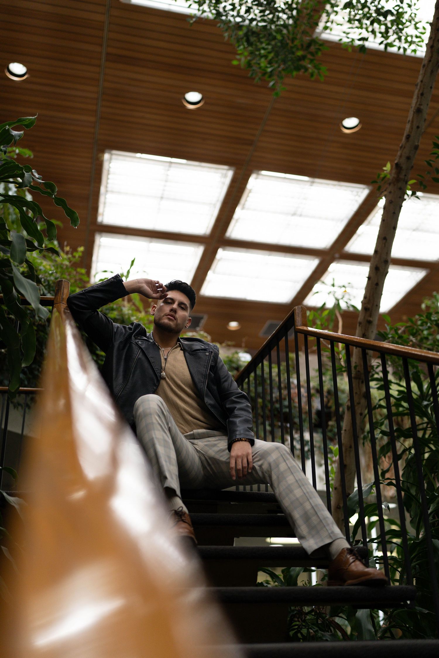 A person lounges on a bench in an indoor garden area with wood paneling and natural lighting.