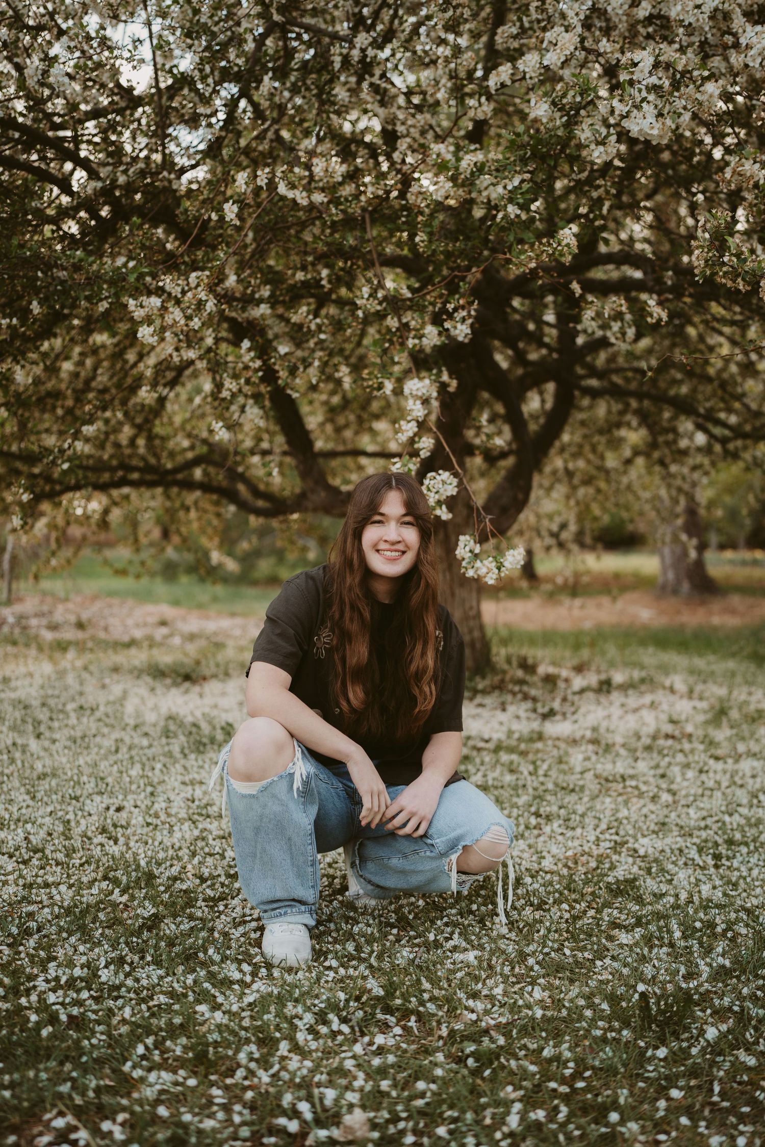 Person sitting in a blooming spring meadow wearing casual denim and white sneakers on a sunny afternoon.