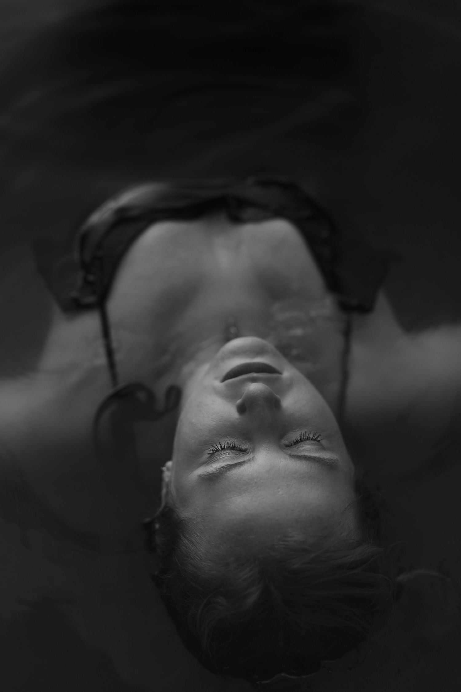 Black and white portrait of a woman floating in water with eyes closed, serene and ethereal mood.