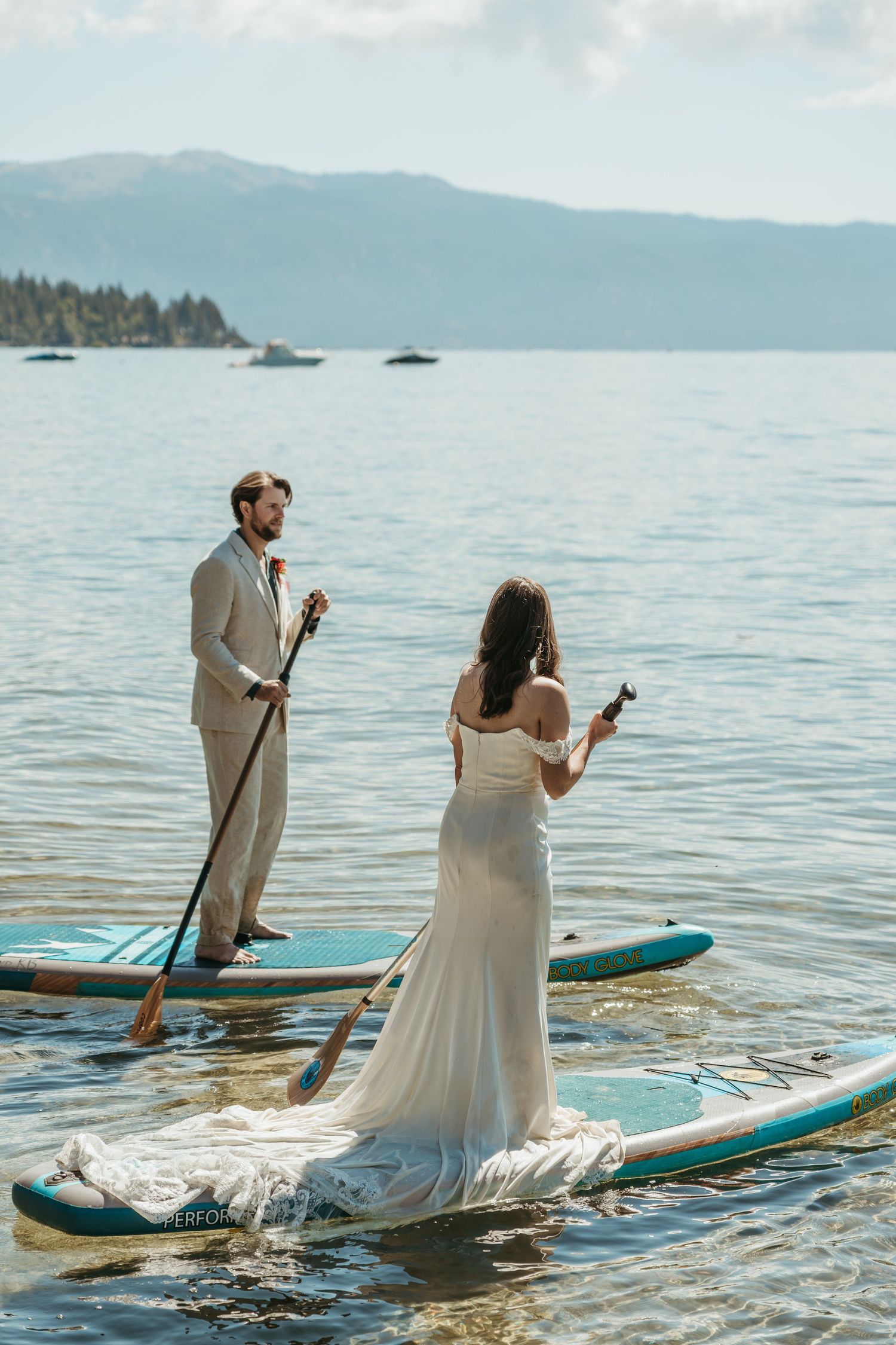 Couple enjoying champagne while standing on paddleboards in Lake Tahoe with mountains in the background.