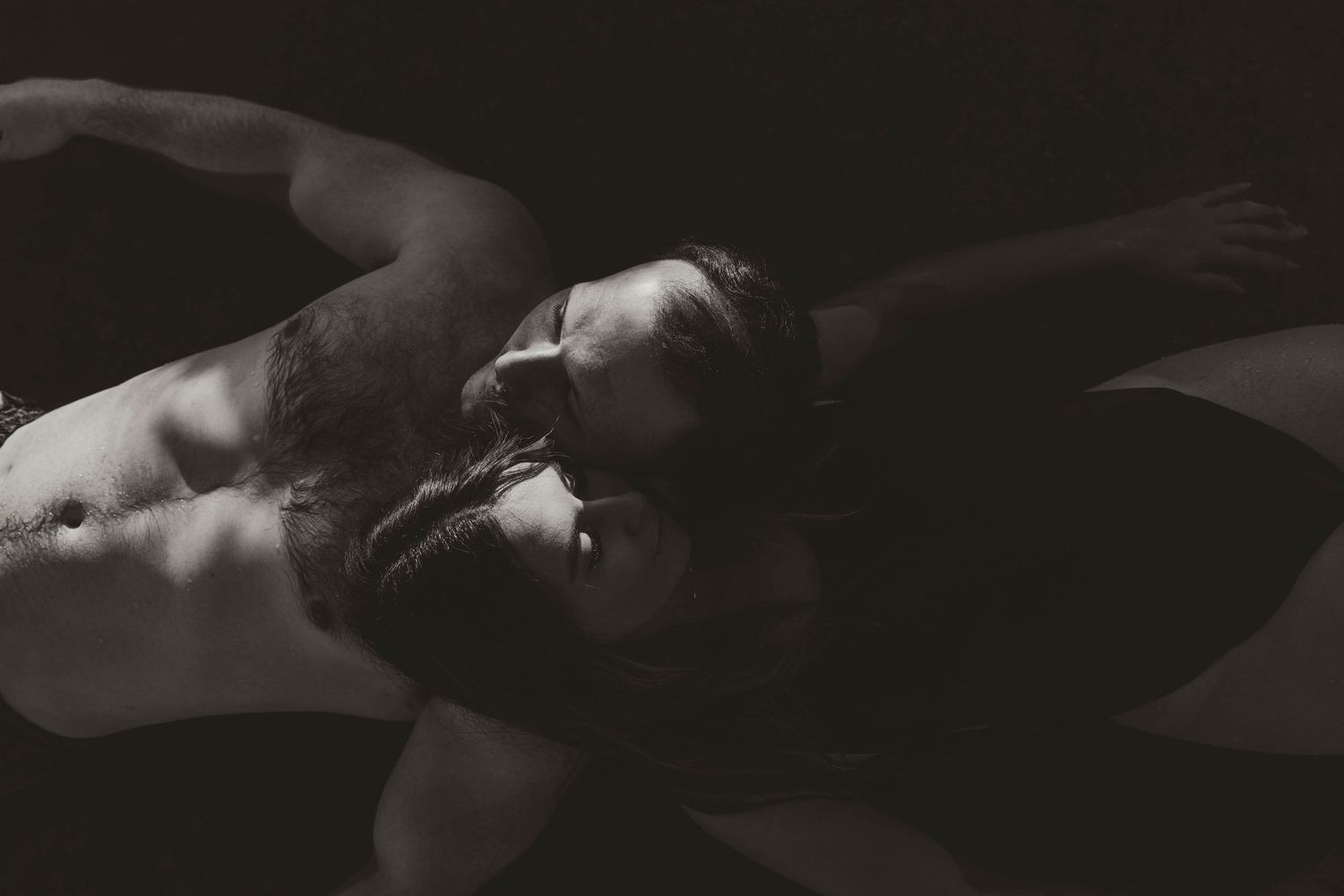 Artistic black and white photograph of two figures in intimate embrace with dramatic shadows and lighting in hot springs.