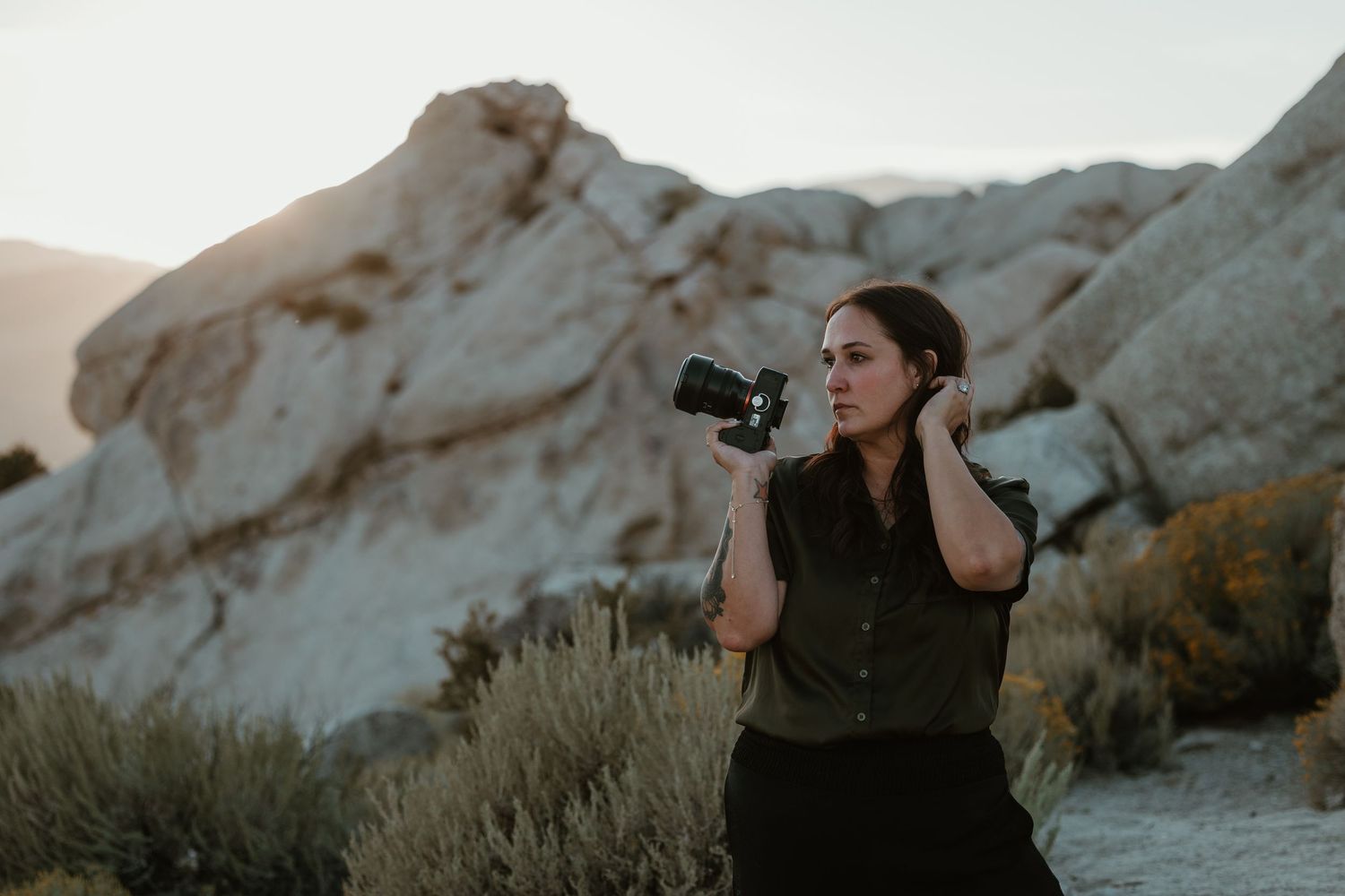 Woman photographer holding camera in rocky desert landscape at dusk.