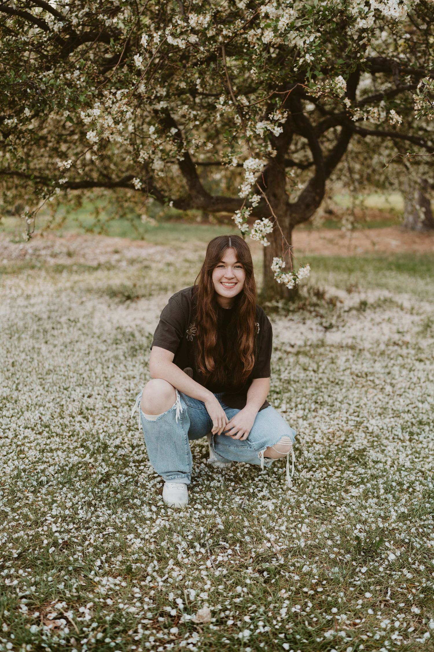 A person sits in a field of white wildflowers wearing jeans and a dark shirt on a spring day.