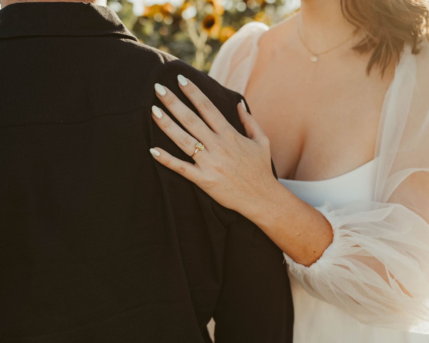 Close-up of a hand with engagement ring resting on man's black shirt during golden hour.
