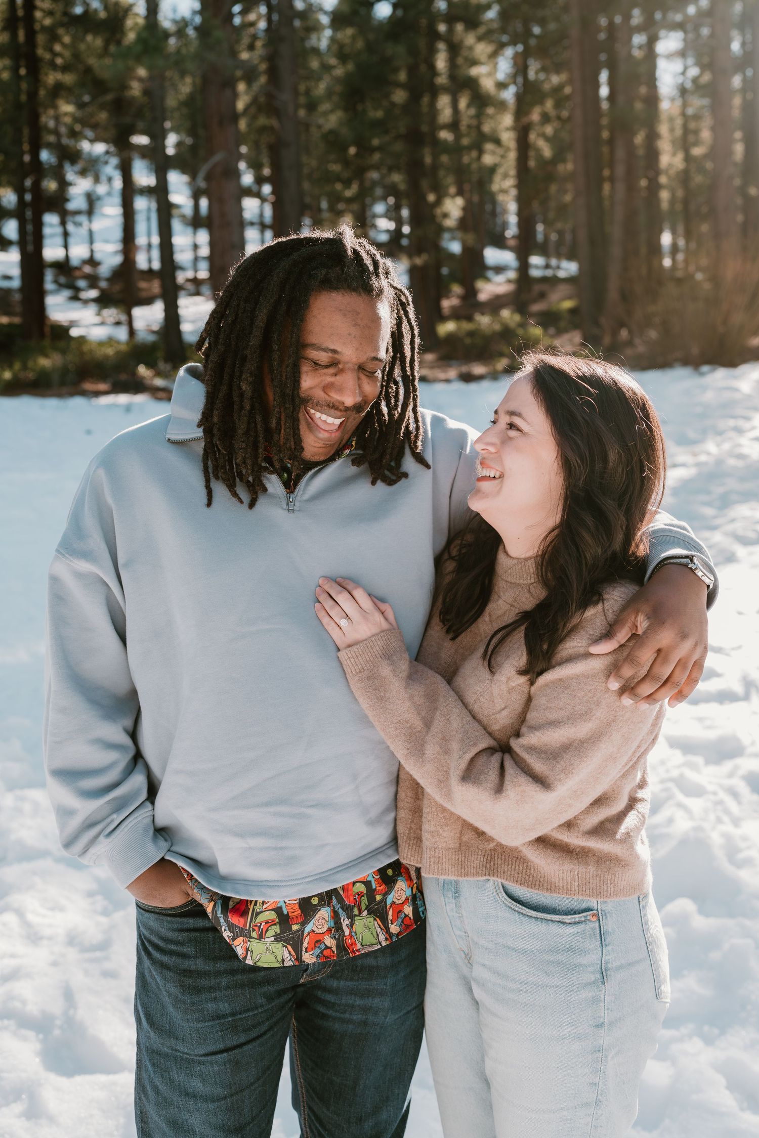 A couple shares intimate moments together in a snowy winter forest setting while wearing casual clothing.