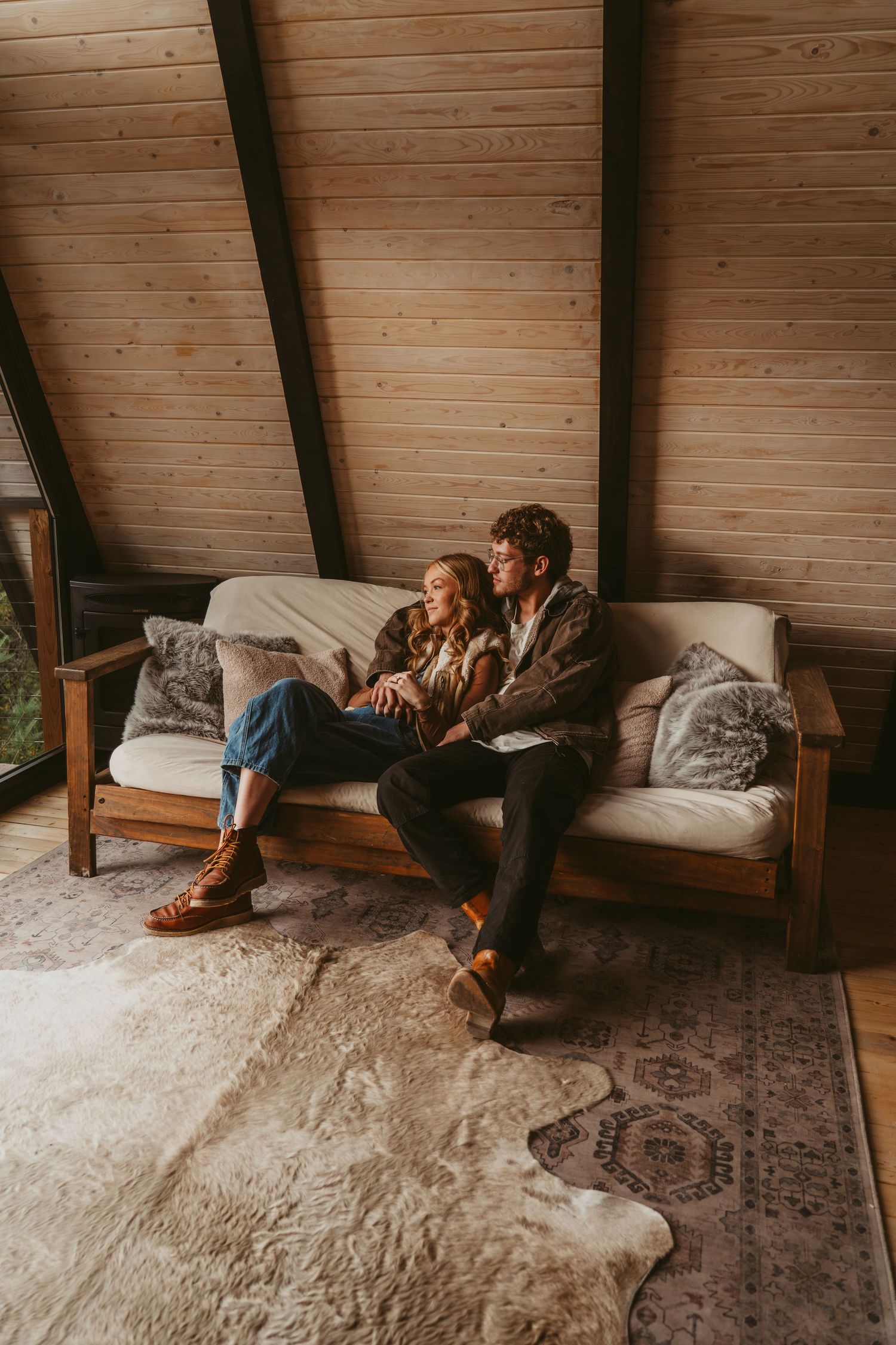 Couple relaxing together on a cozy wooden couch in a rustic cabin with exposed beams and patterned rug.