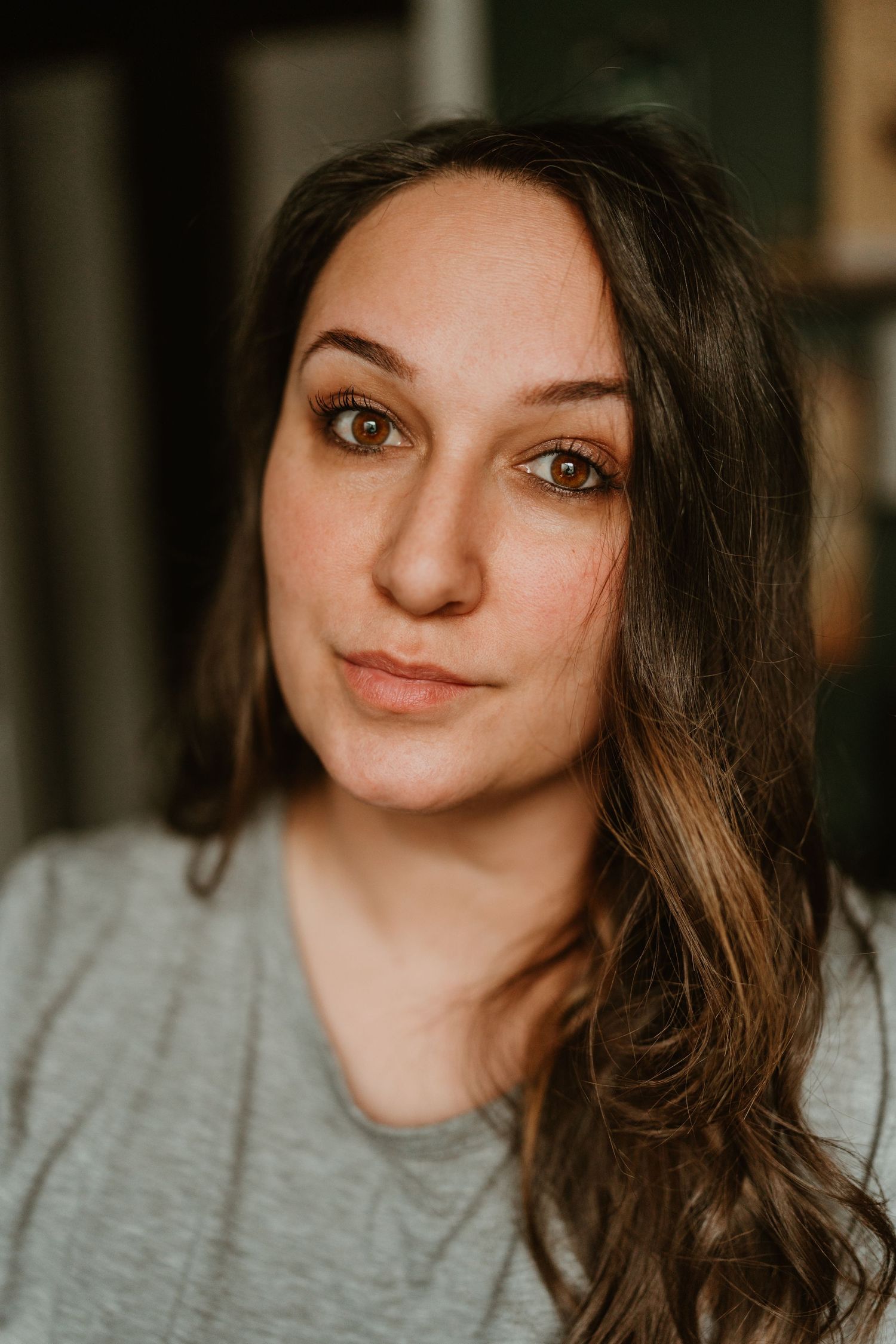 Close-up portrait of a young woman with long brown hair and hazel eyes wearing a gray t-shirt.