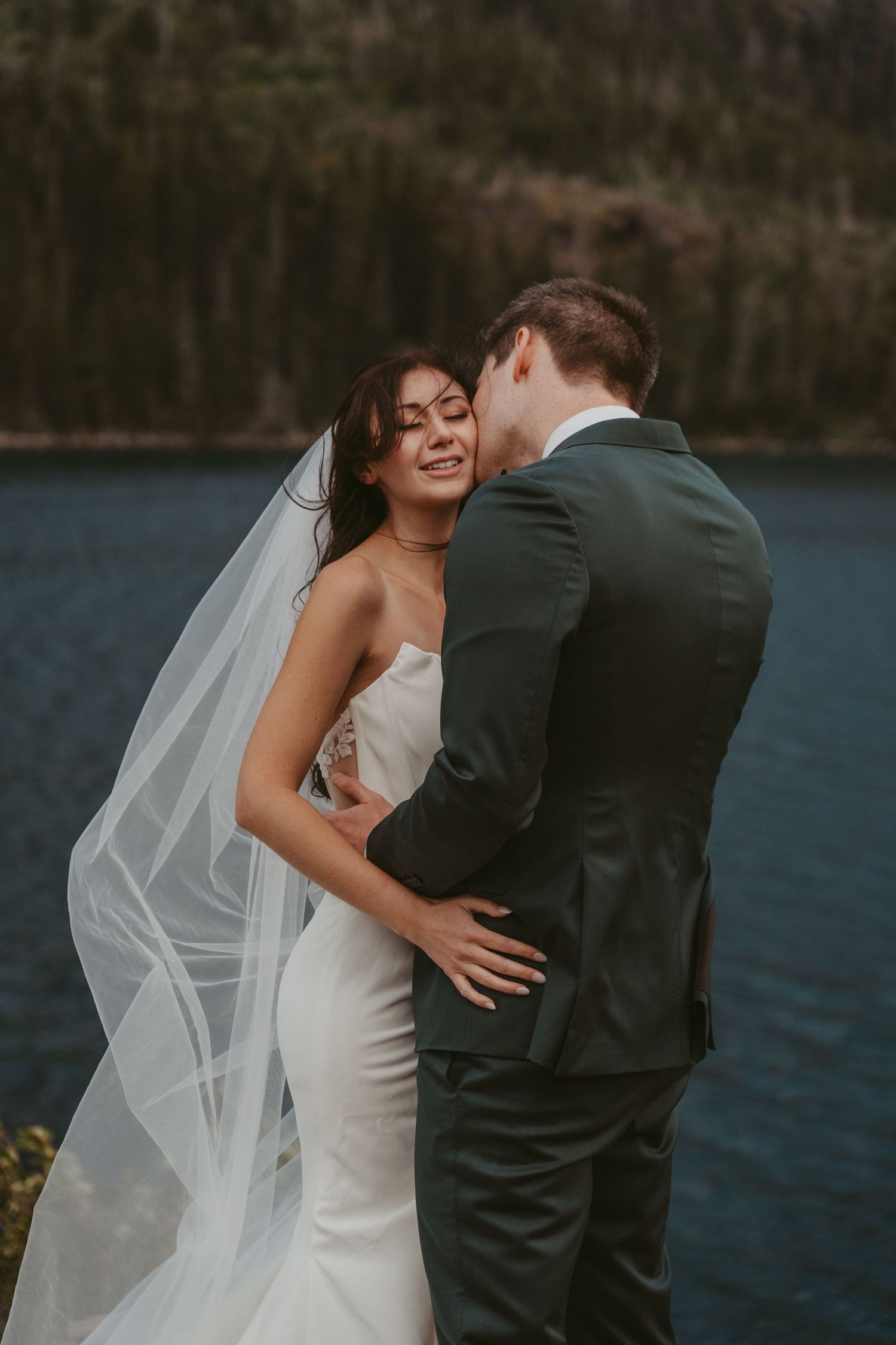 A romantic wedding couple embraces by a scenic lakeside during their first look moment in nature.