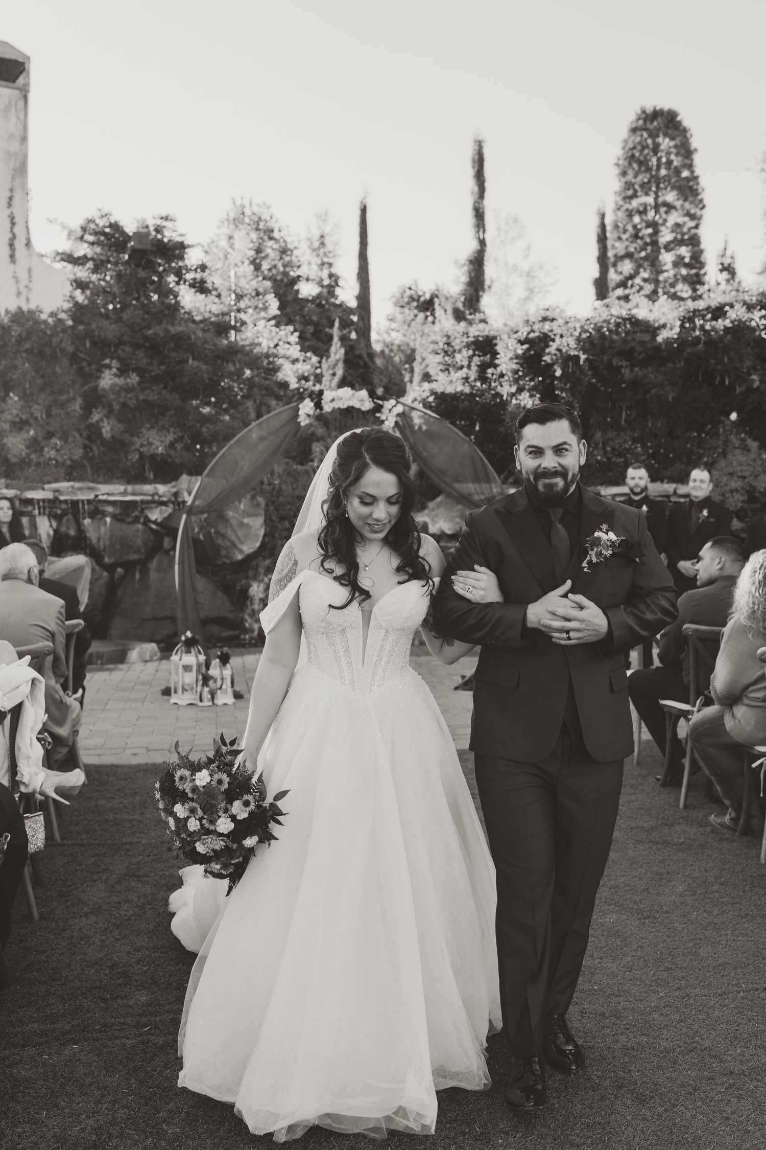 Black and white photo series showing a couple walking down the aisle at an outdoor wedding celebration on a grassy lawn.
