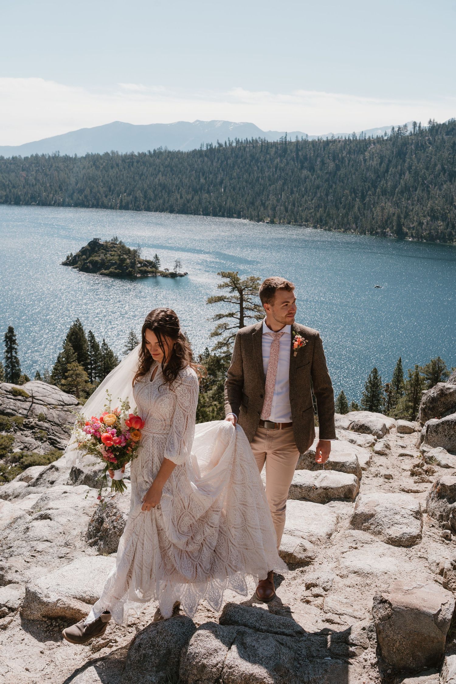 Bride and groom walking on rocky steps at Lake Tahoe Emerald Bay overlook on wedding day.