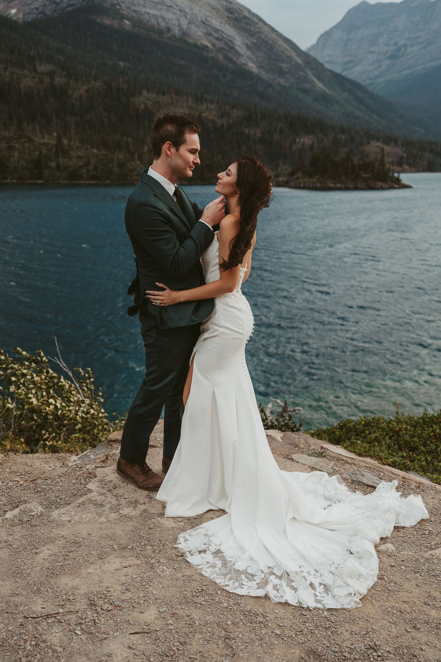 A couple shares a romantic moment on a cliff overlooking a scenic mountain lake in a stunning outdoor wedding setting.