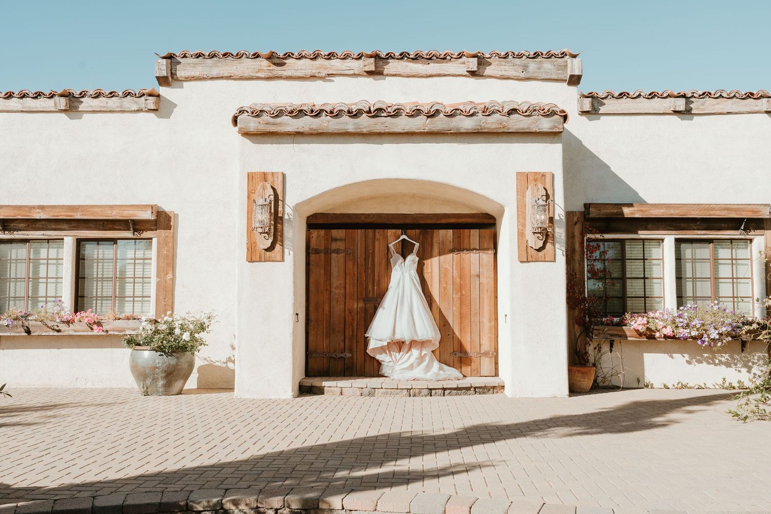 A flowing white wedding dress hangs in the doorway of a Spanish-style stucco building with terracotta accents.
