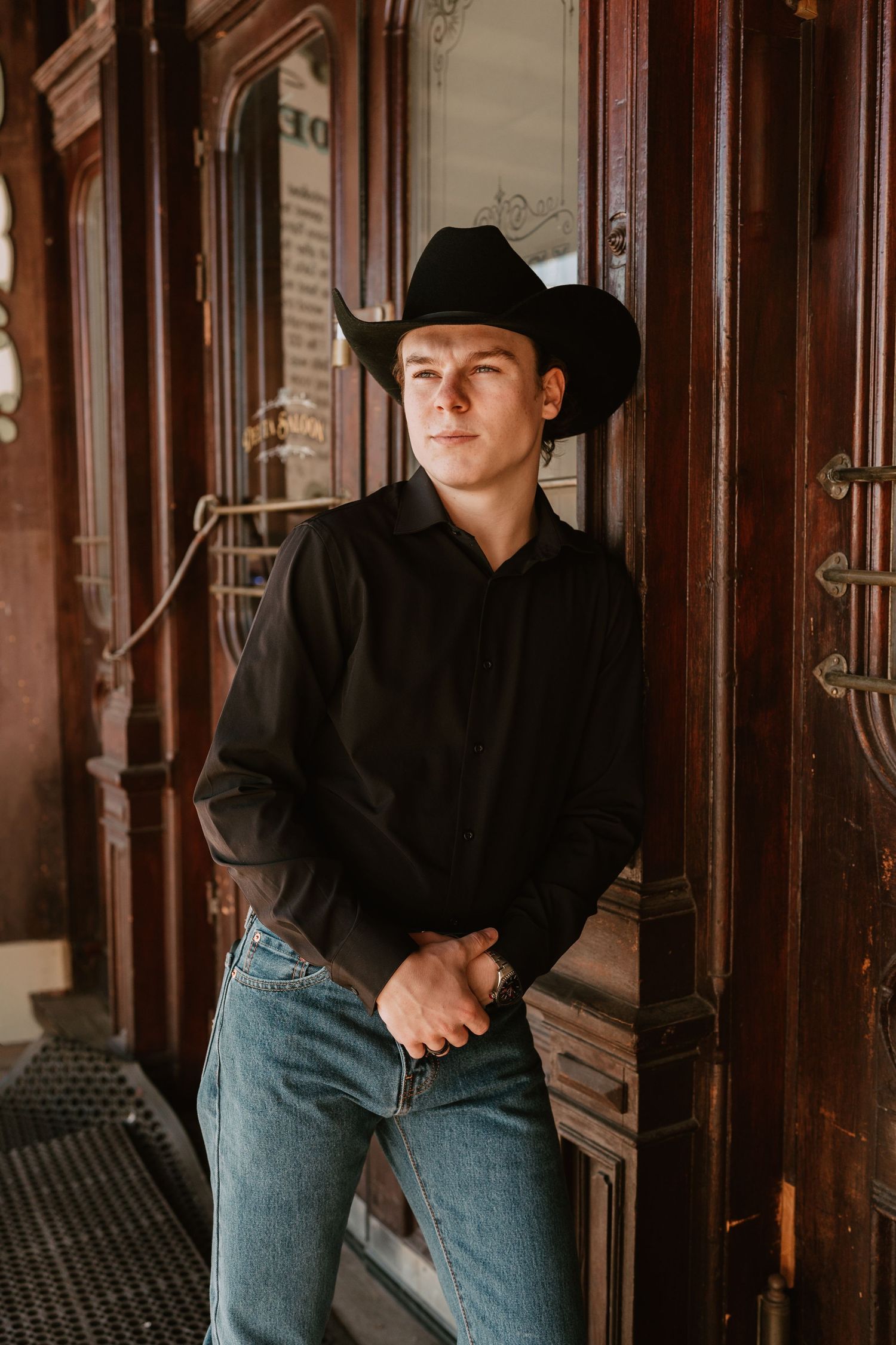 Figure in western wear poses dramatically against vintage wooden architecture.