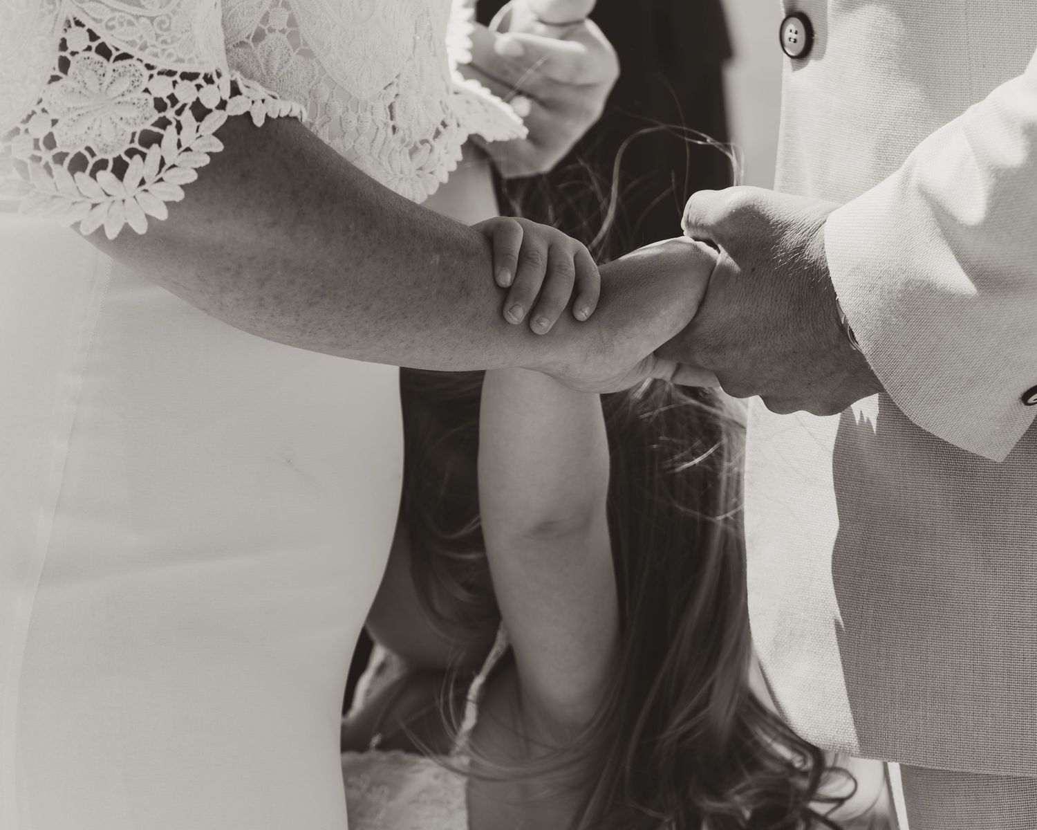 A black and white photograph shows a couple holding hands with their daughter during thier wedding ceremony.