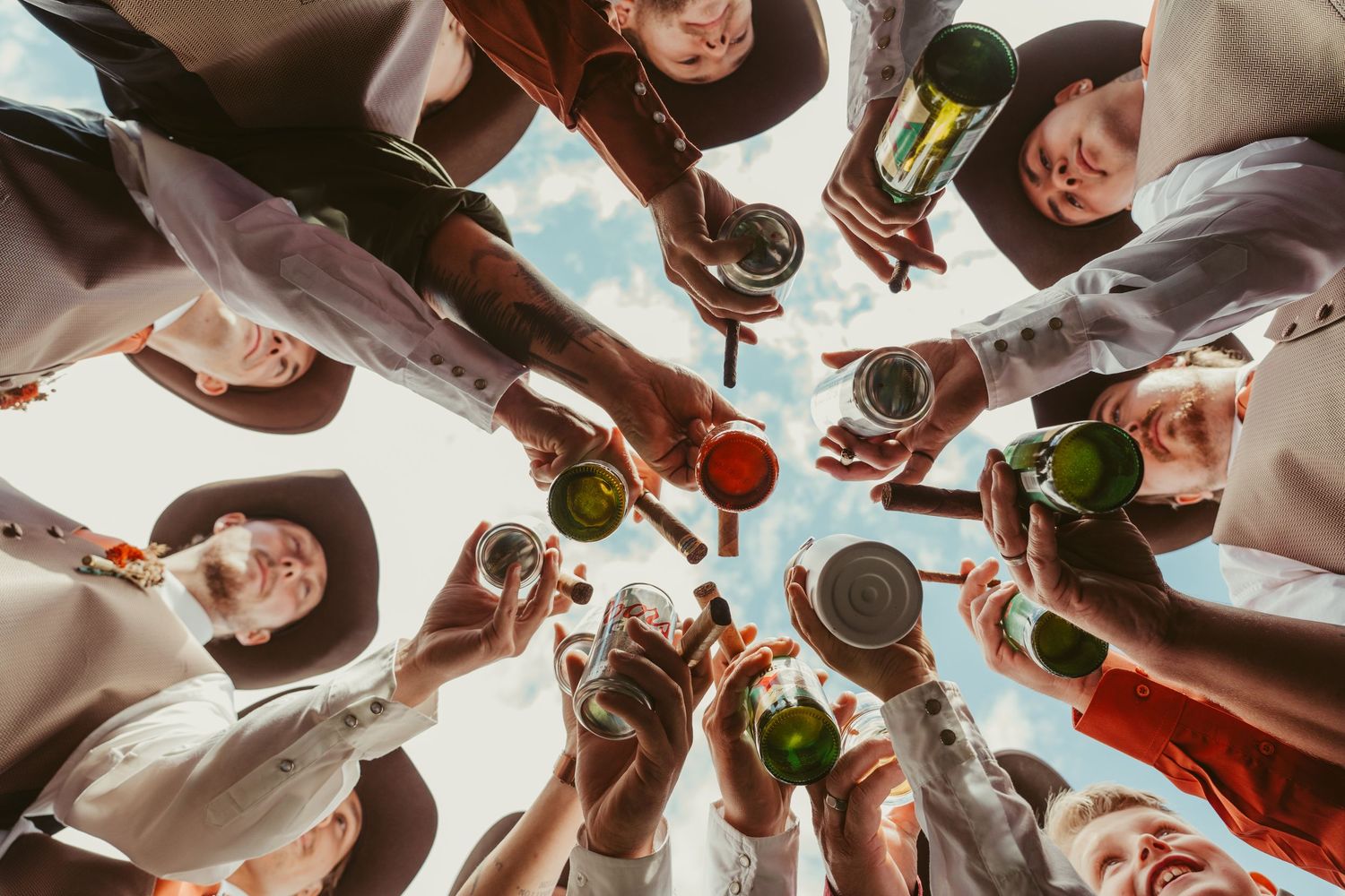 A low-angle view of people holding wine bottles and glasses in a celebratory toast against a bright sky.